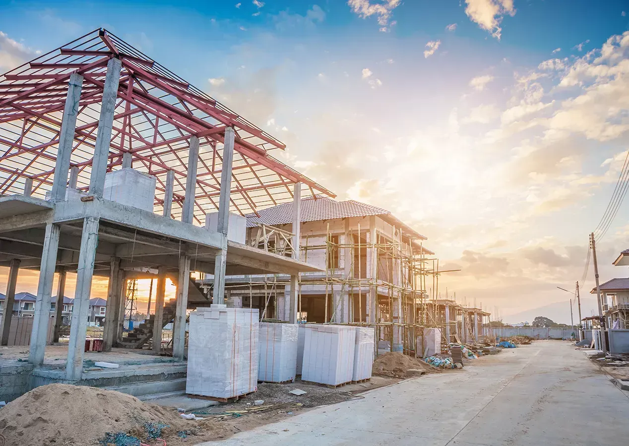 A residential construction site at sunset with unfinished concrete homes and exposed metal roof framing.