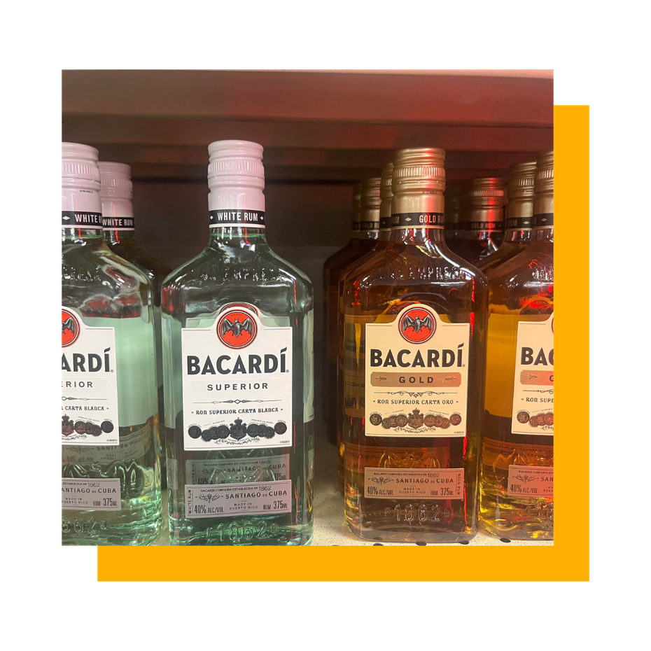 Bacardi rum bottles in a store. Clear, black, and gold labels; white and gold bottle caps.