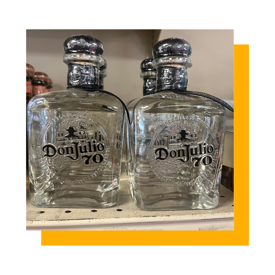 Two bottles of Don Julio 70 tequila on a shelf with other bottles in the background.