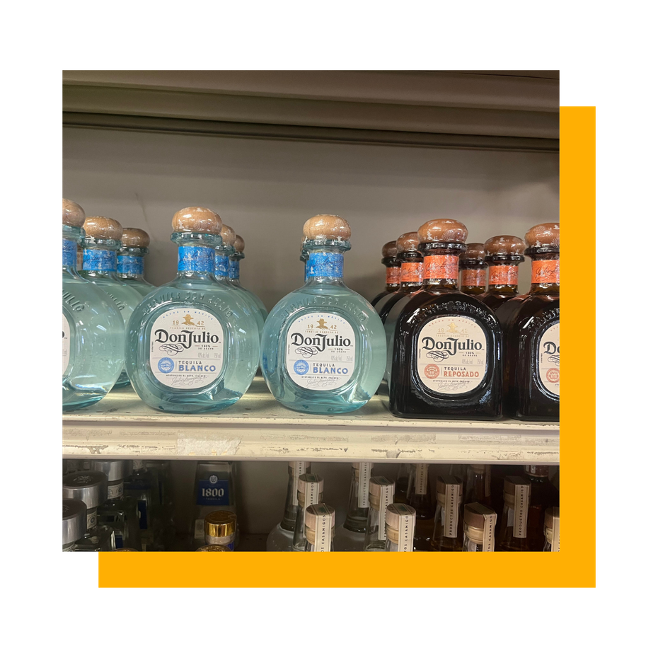 Bottles of Don Julio tequila on shelves in a store. The bottles are blue, black, and brown.
