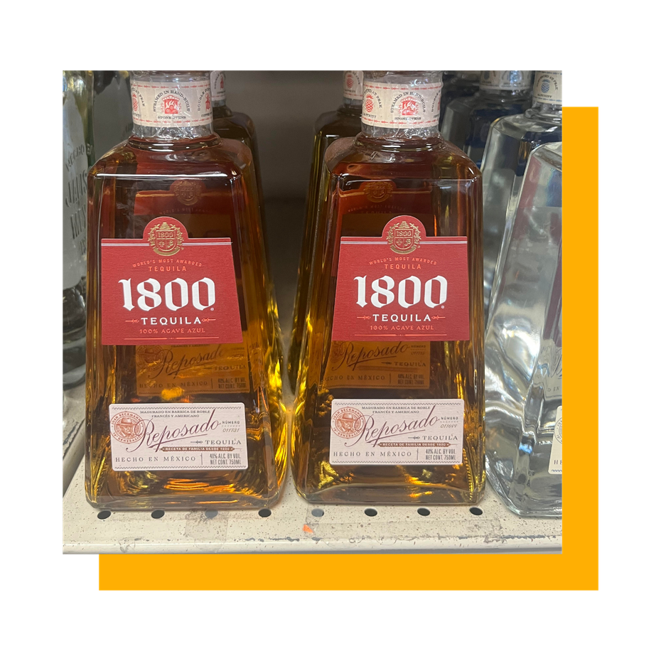 Two bottles of 1800 Tequila, amber liquid in square bottles with red and white labels, on a shelf.