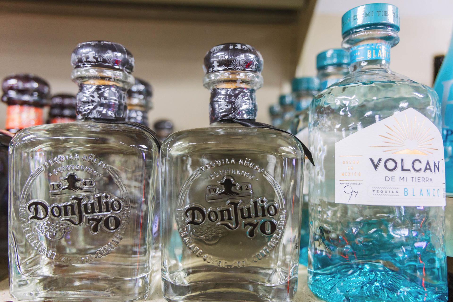 Bottles of tequila on a shelf: Don Julio 70 and Volcan, with clear bottles, silver caps, and labels.