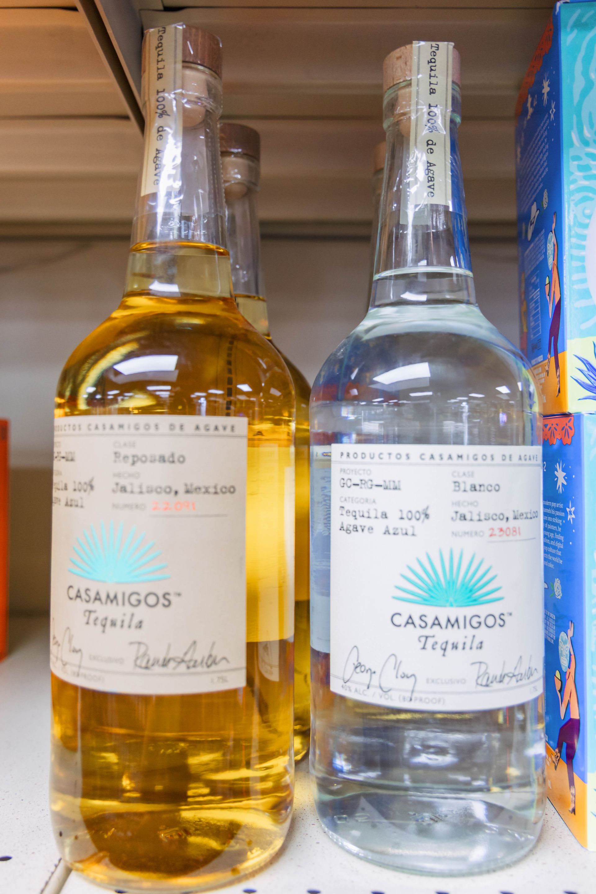 Two bottles of Casamigos tequila on a shelf; one gold, one clear, both labeled.
