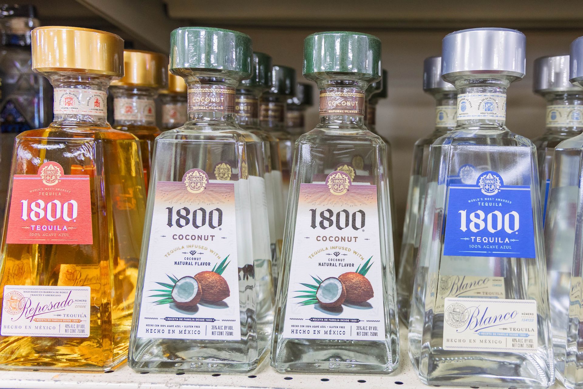 Bottles of 1800 Tequila in various flavors, including pineapple and coconut, on a shelf.