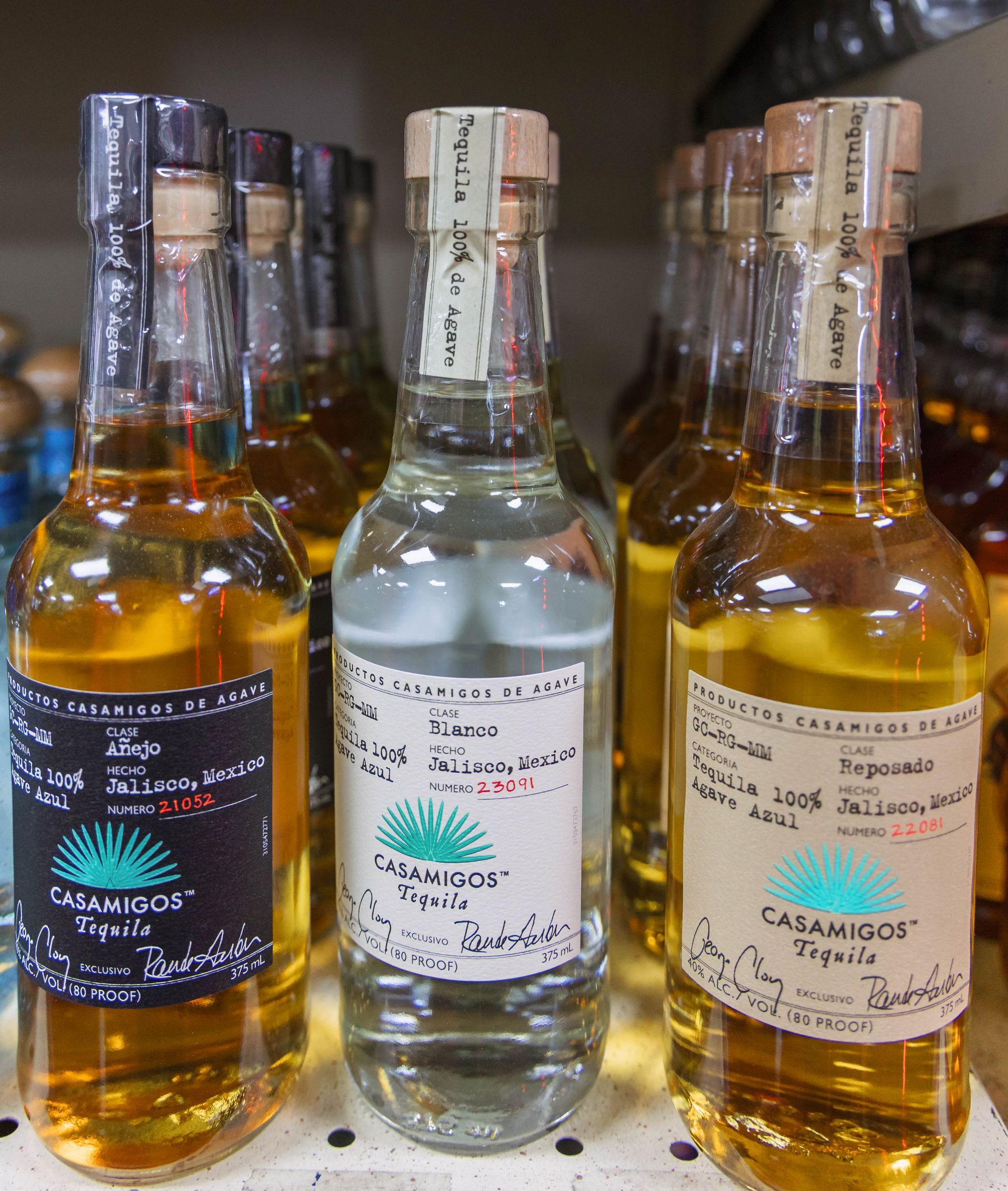 Bottles of Casamigos tequila on a shelf; clear and amber liquids, various labels.