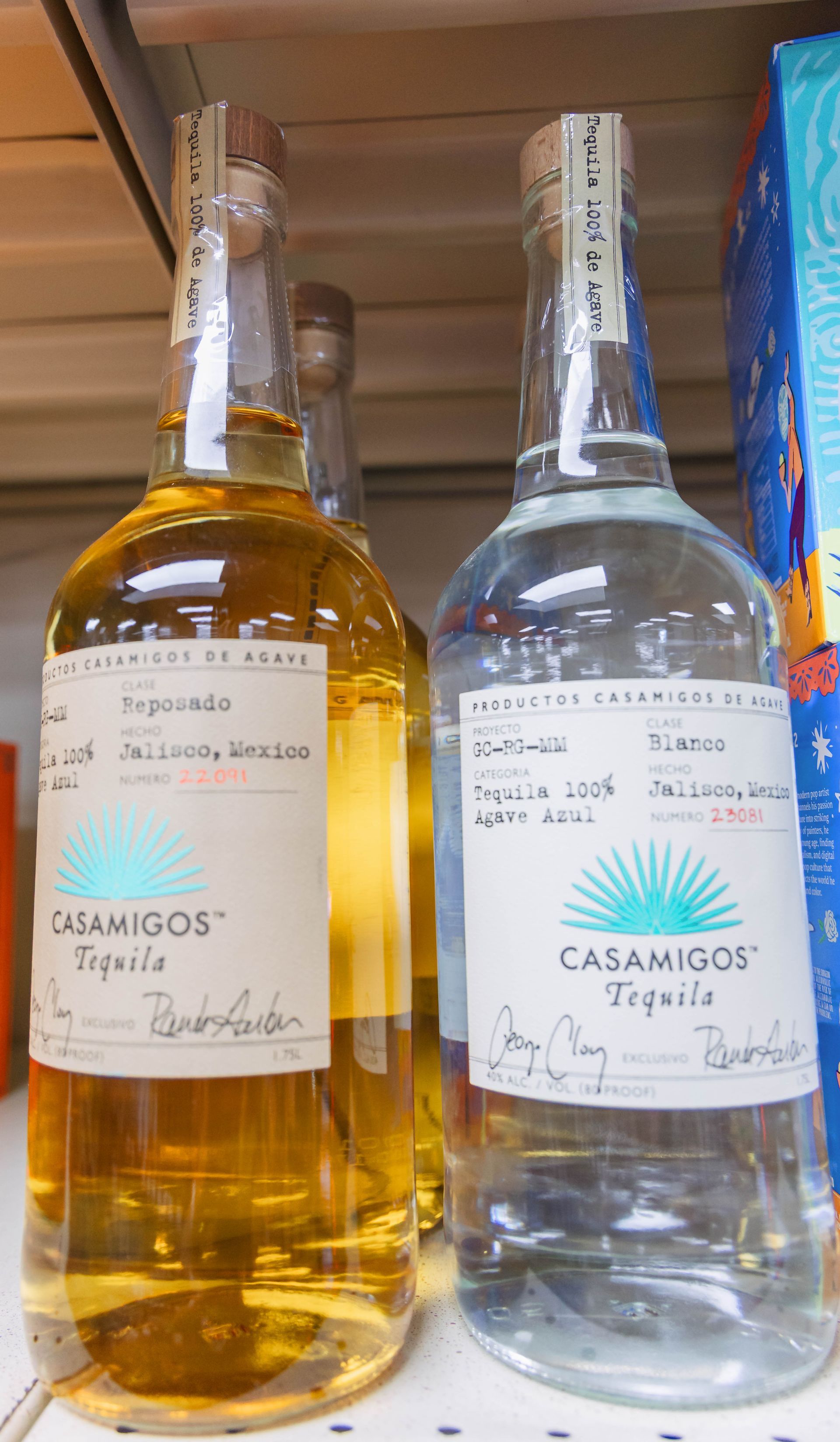 Two Casamigos tequila bottles: Blanco and Reposado, on a liquor store shelf.