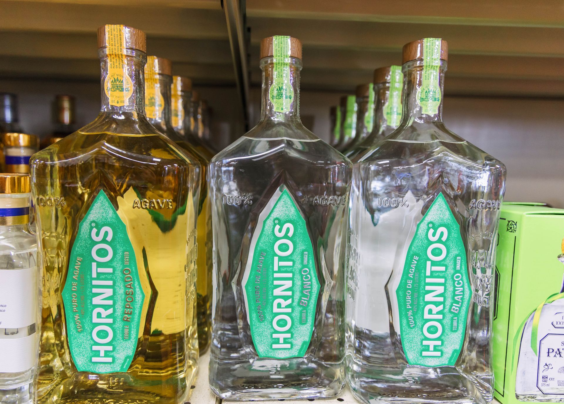 Bottles of Hornitos tequila on a shelf; two clear, one golden, with green and white labels.