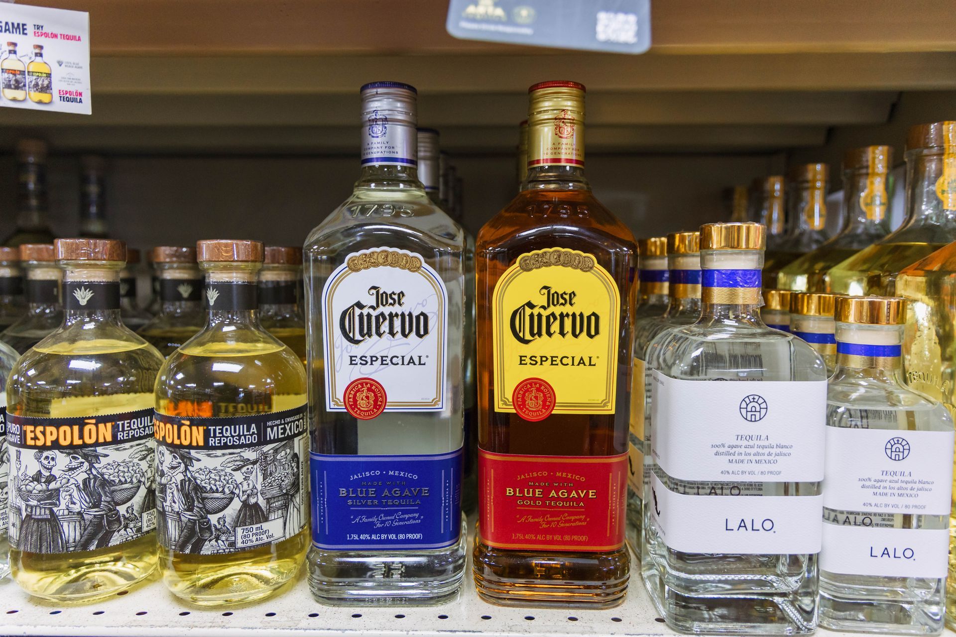 Bottles of various tequilas on a store shelf. Includes clear and amber tequila bottles.