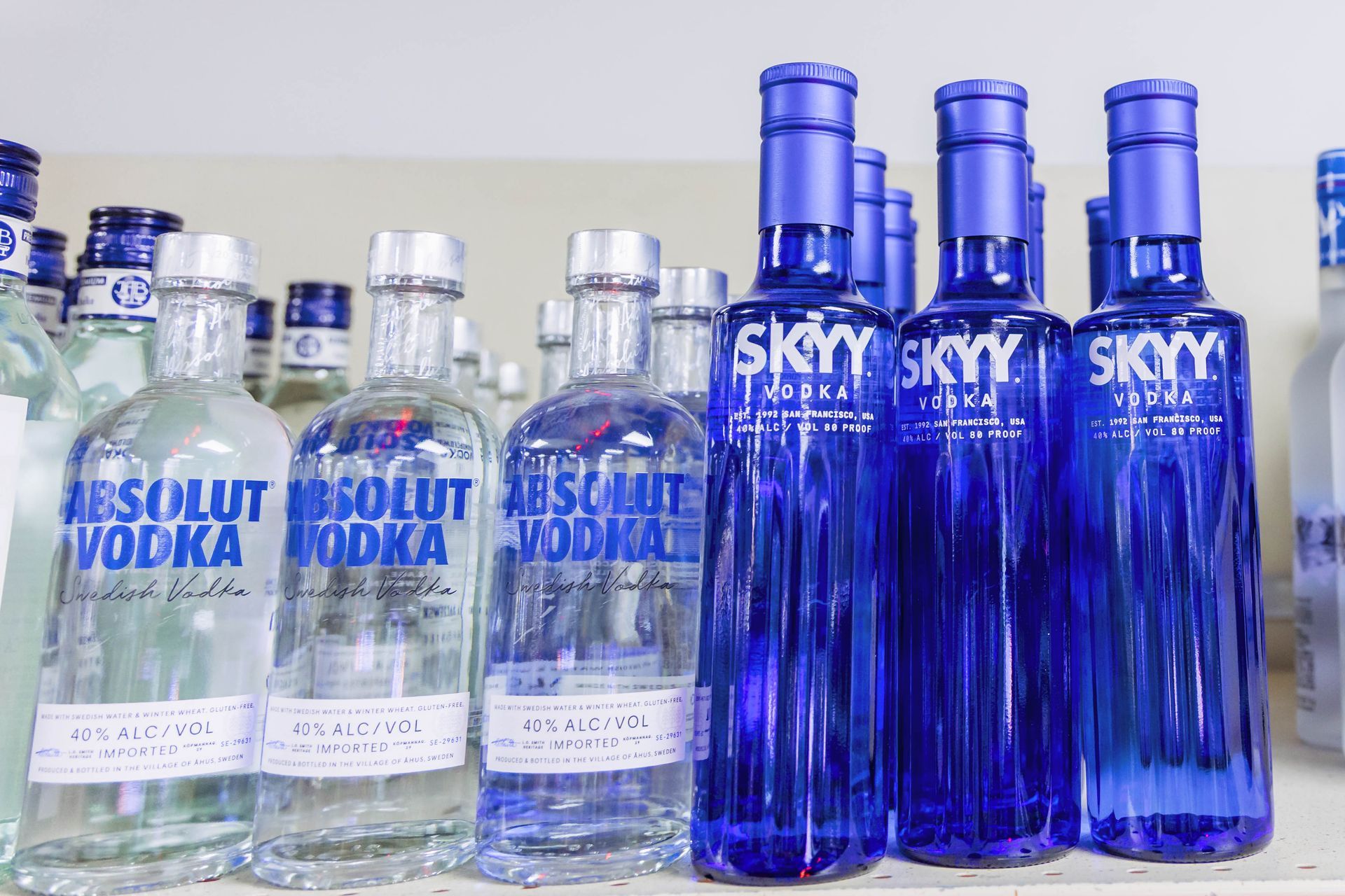 Bottles of Absolut Vodka and Skyy Vodka on a shelf; blue, clear glass bottles.