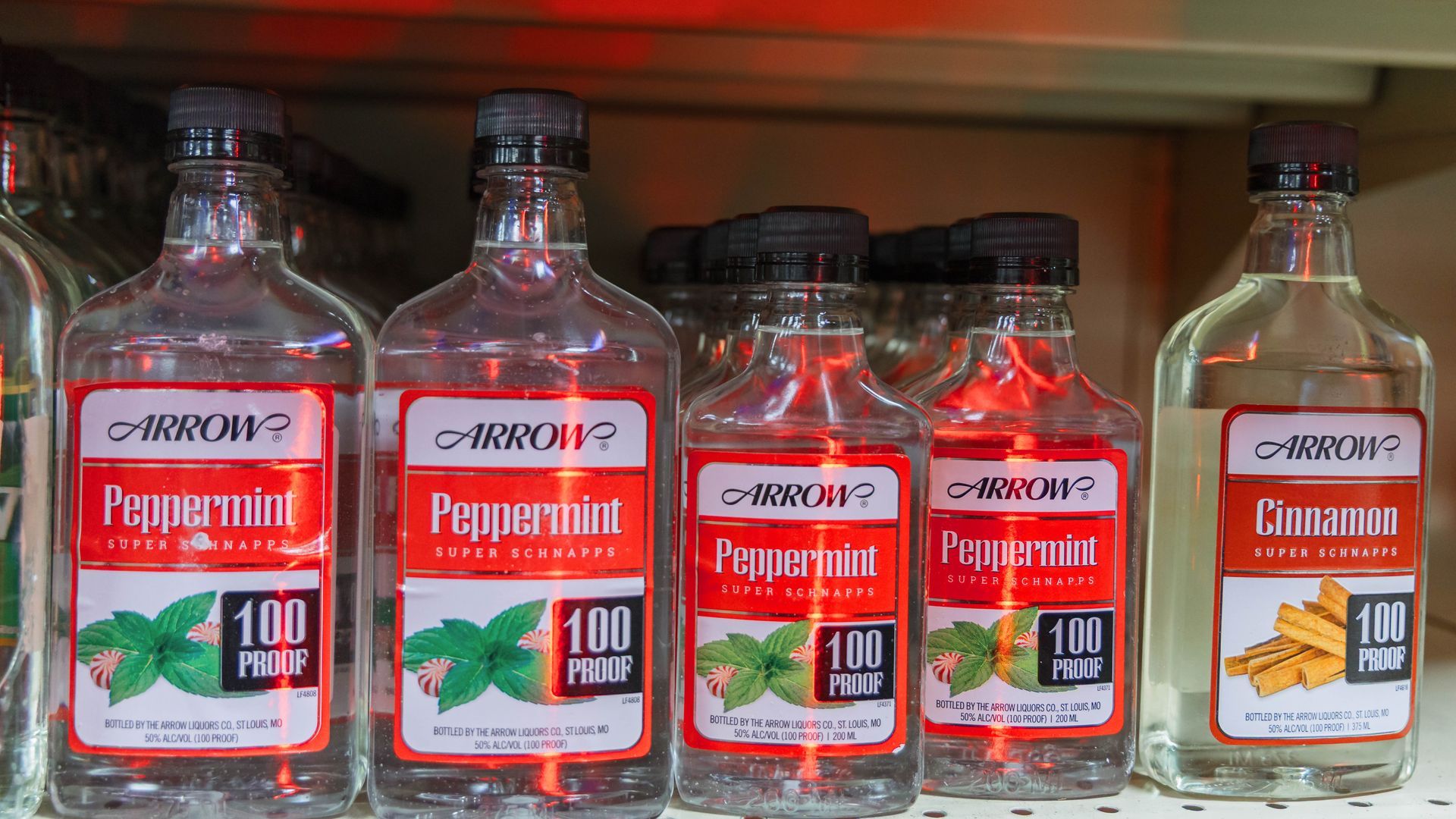 Bottles of Arrow peppermint and cinnamon schnapps, 100 proof, on a shelf.