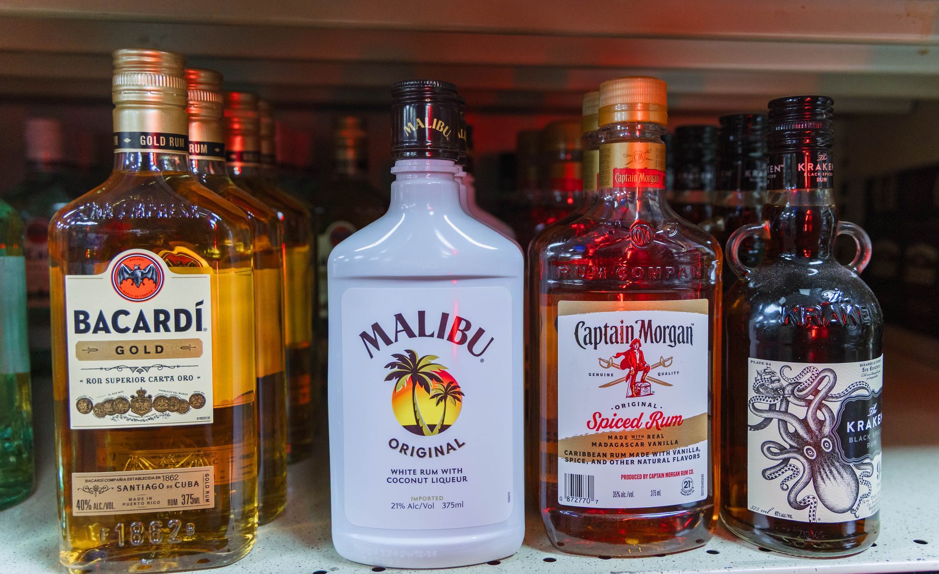Bottles of liquor including Bacardi Gold, Malibu, and Captain Morgan's rum on a shelf.