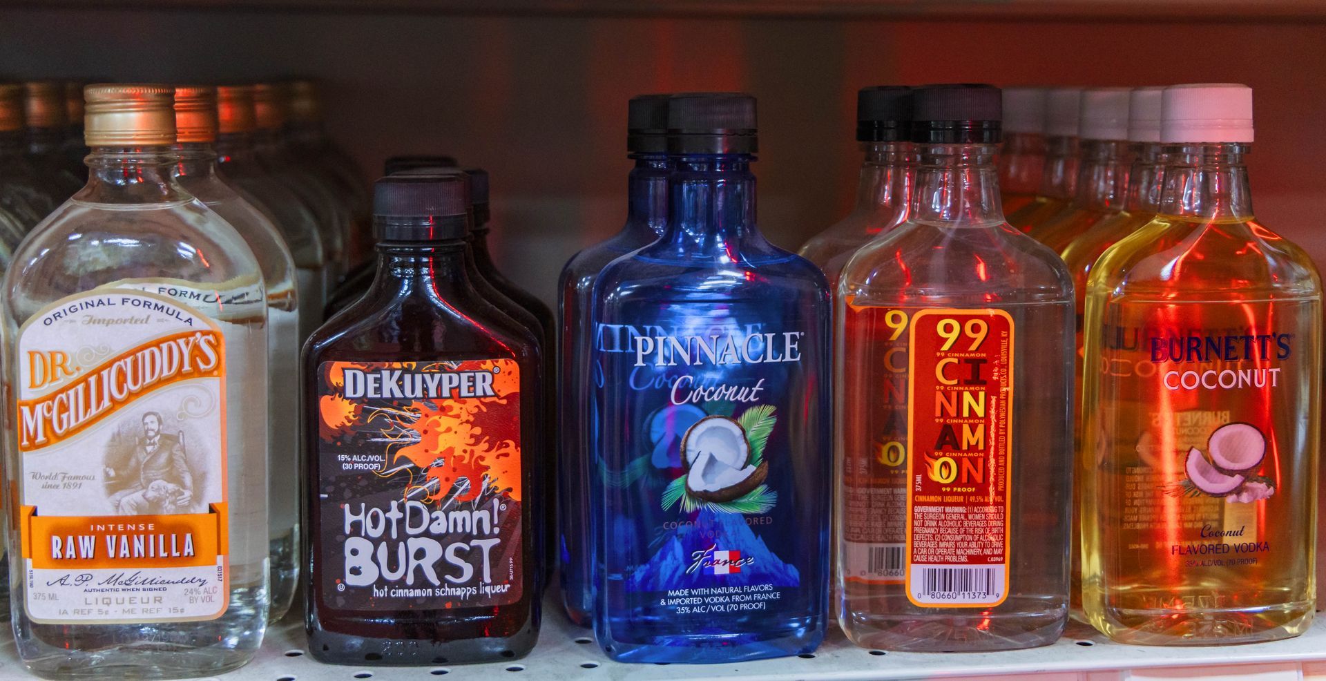 Bottles of various colored liquor on a shelf, including vanilla, fiery, blue coconut, and orange.