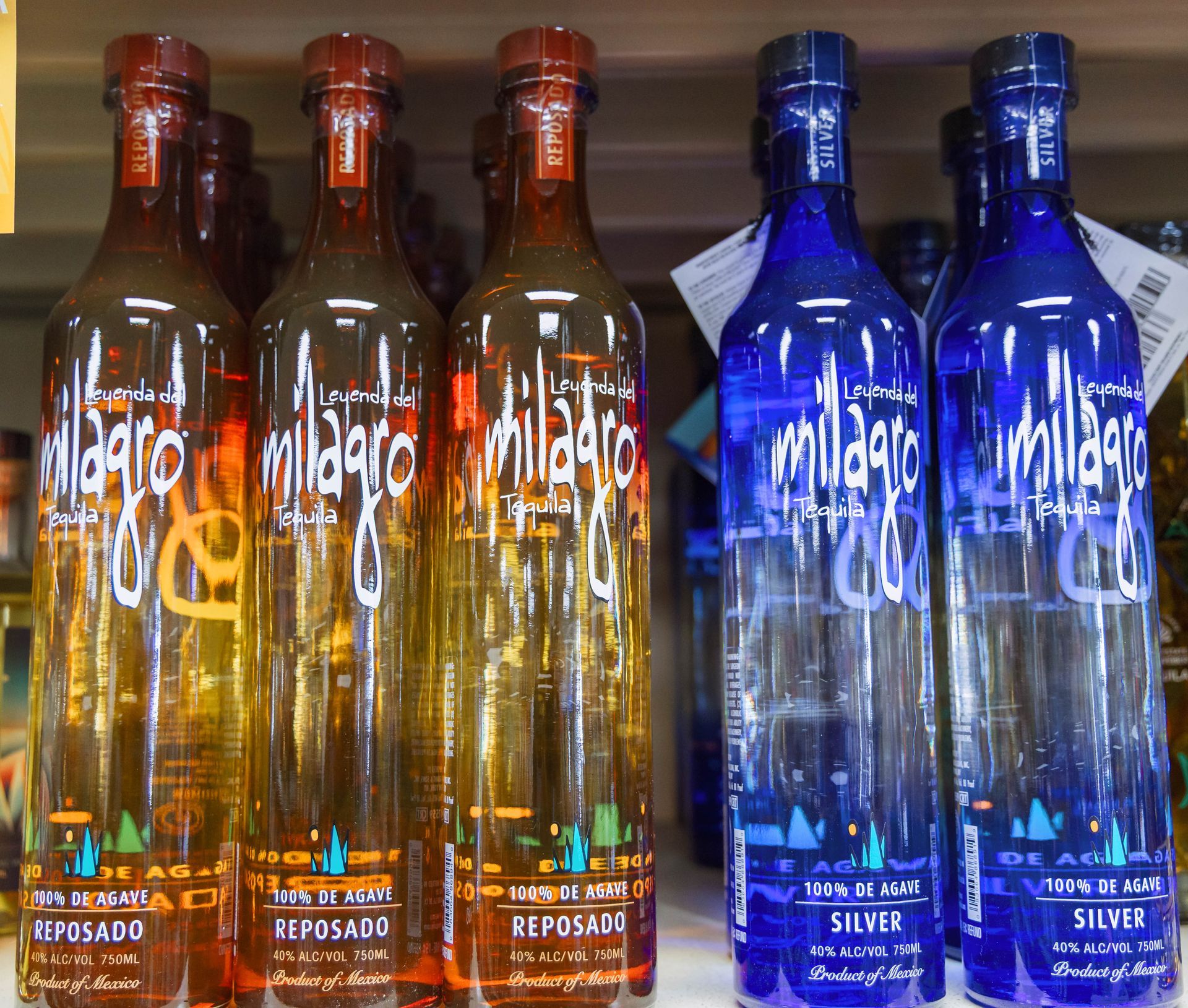 Bottles of Milagro tequila: Reposado (amber) and Silver (blue) on a shelf.