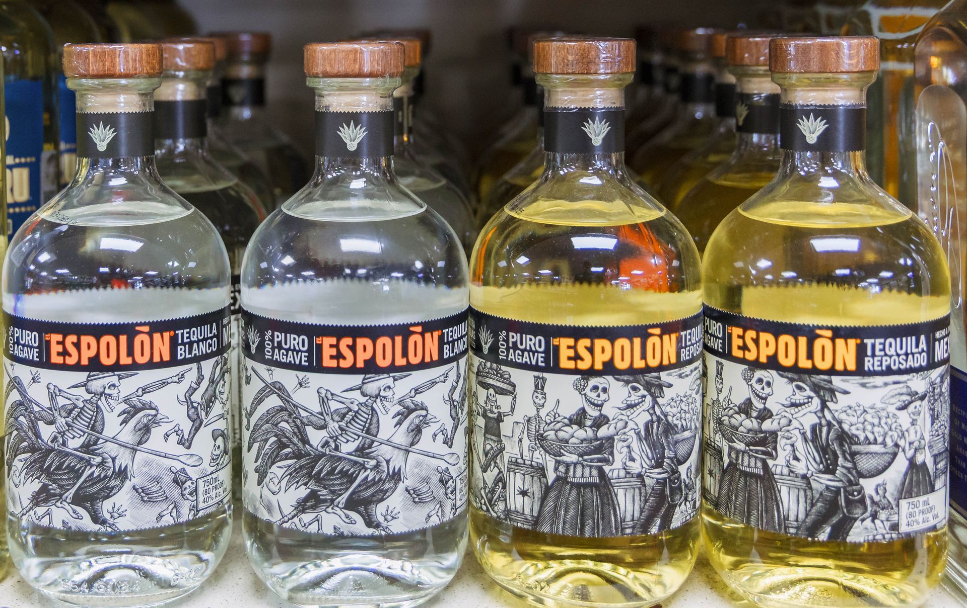 Four bottles of Espolòn tequila, ranging from clear to golden, on a store shelf.