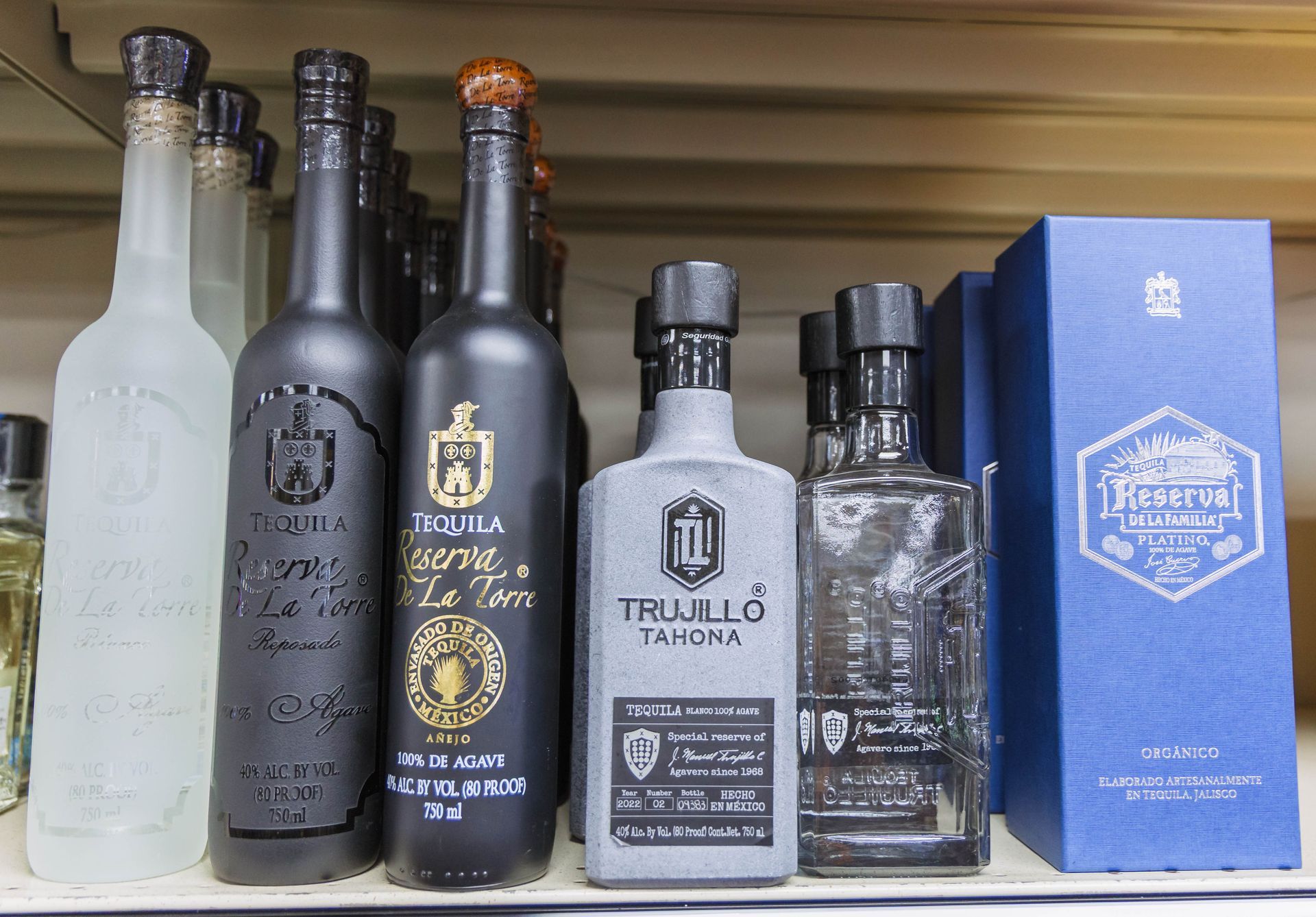 Bottles of tequila in various colors and shapes on a shelf at a liquor store.