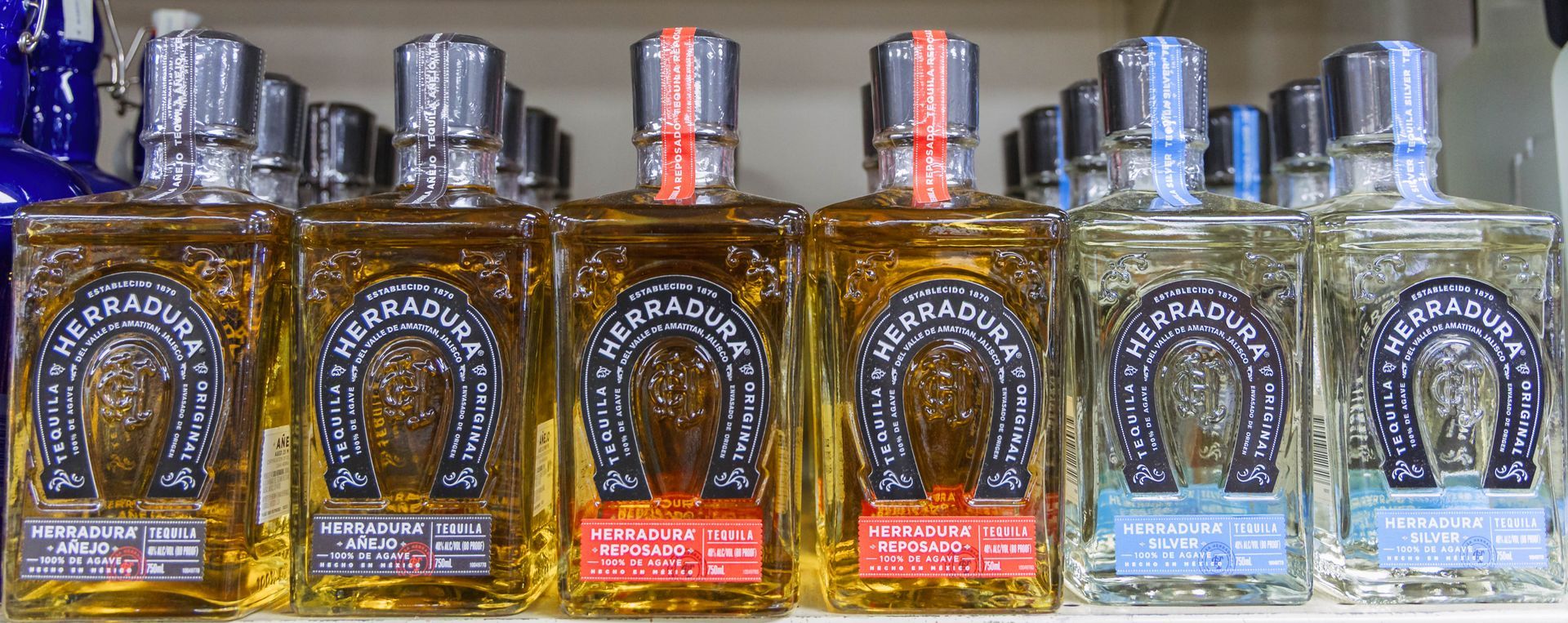 Bottles of tequila lined up on a shelf, silver and red accents, square shape.
