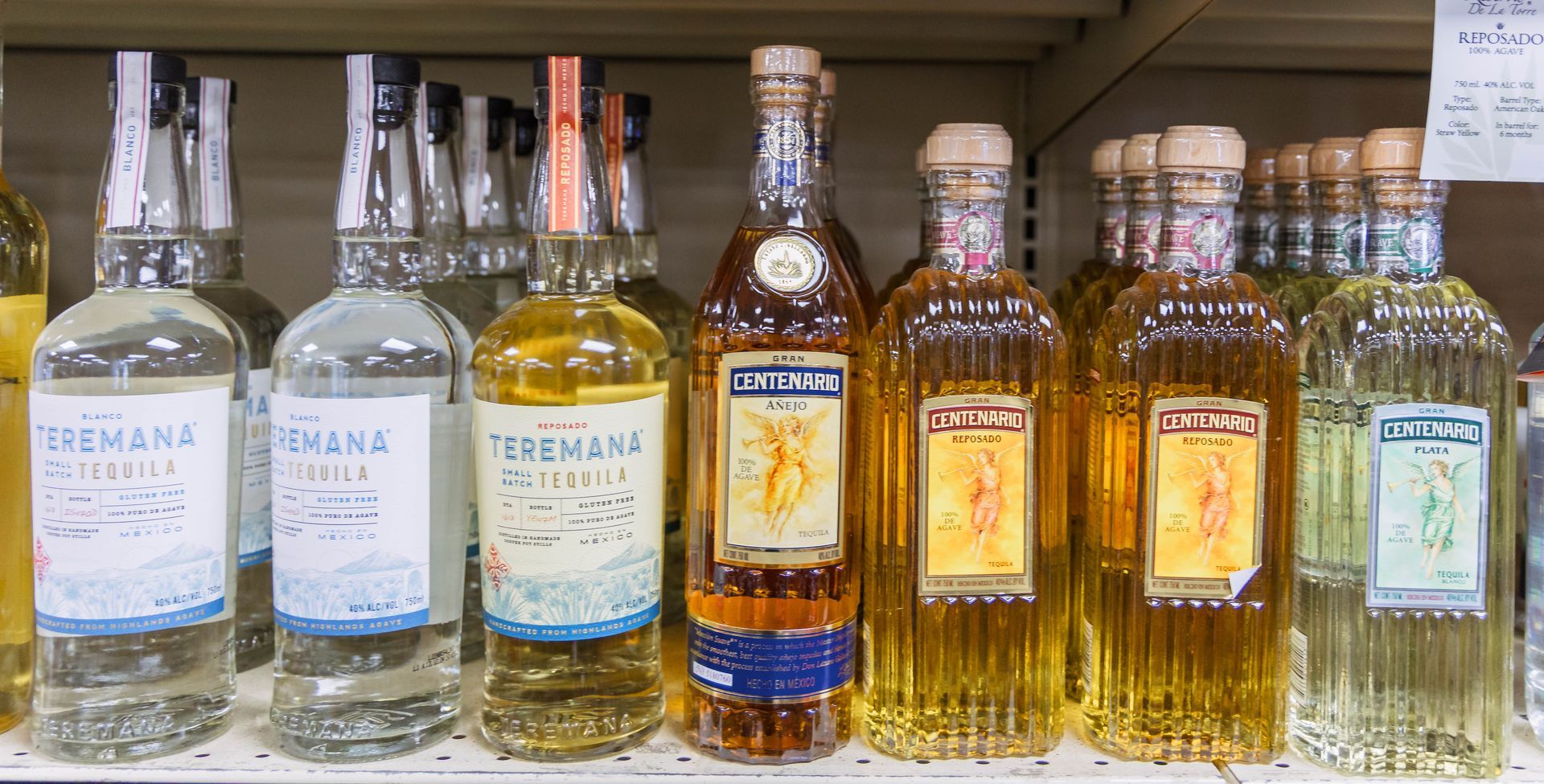 Bottles of tequila on a shelf, varying colors, labels visible, store setting.