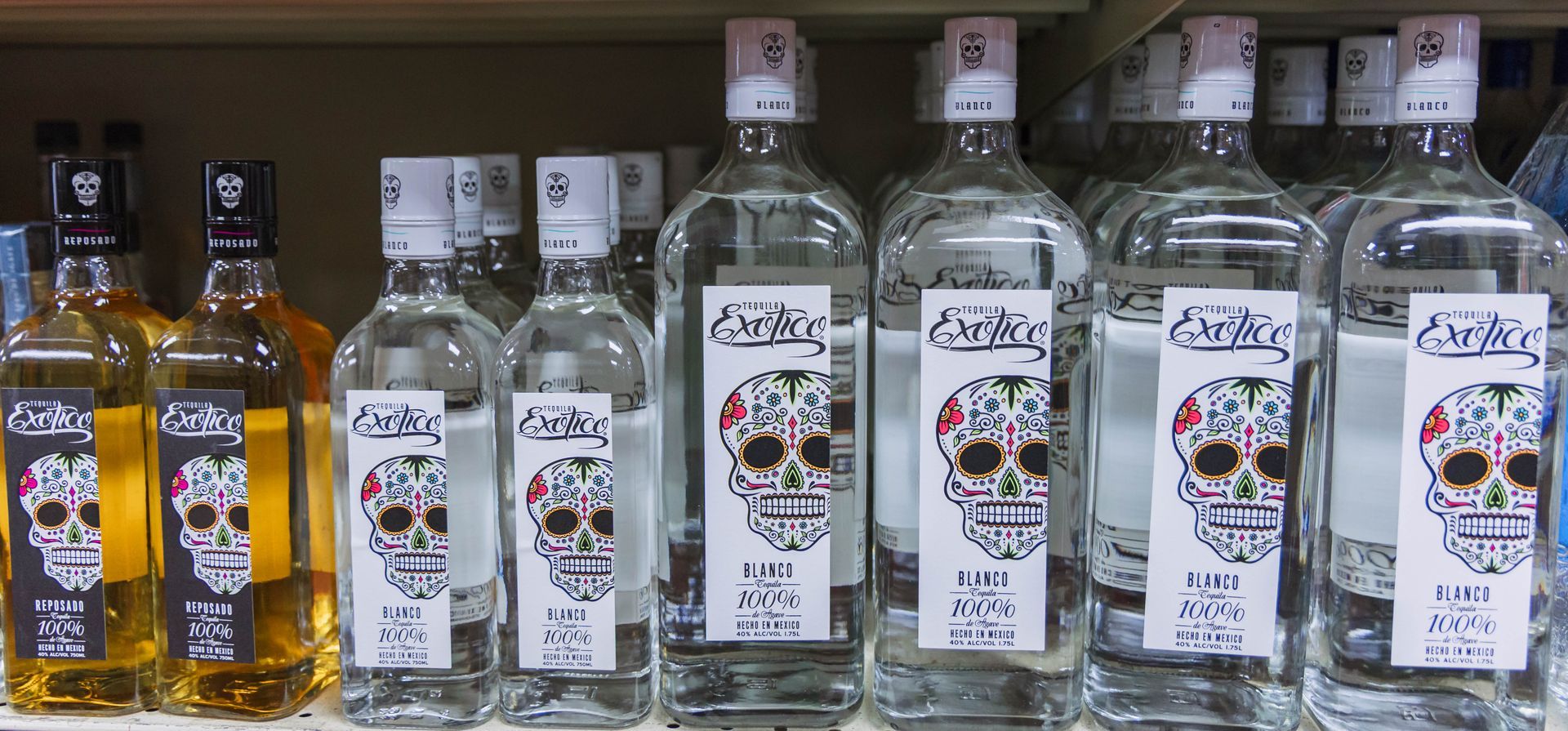 Bottles of tequila on a shelf, some are clear, some are amber, with skull labels.