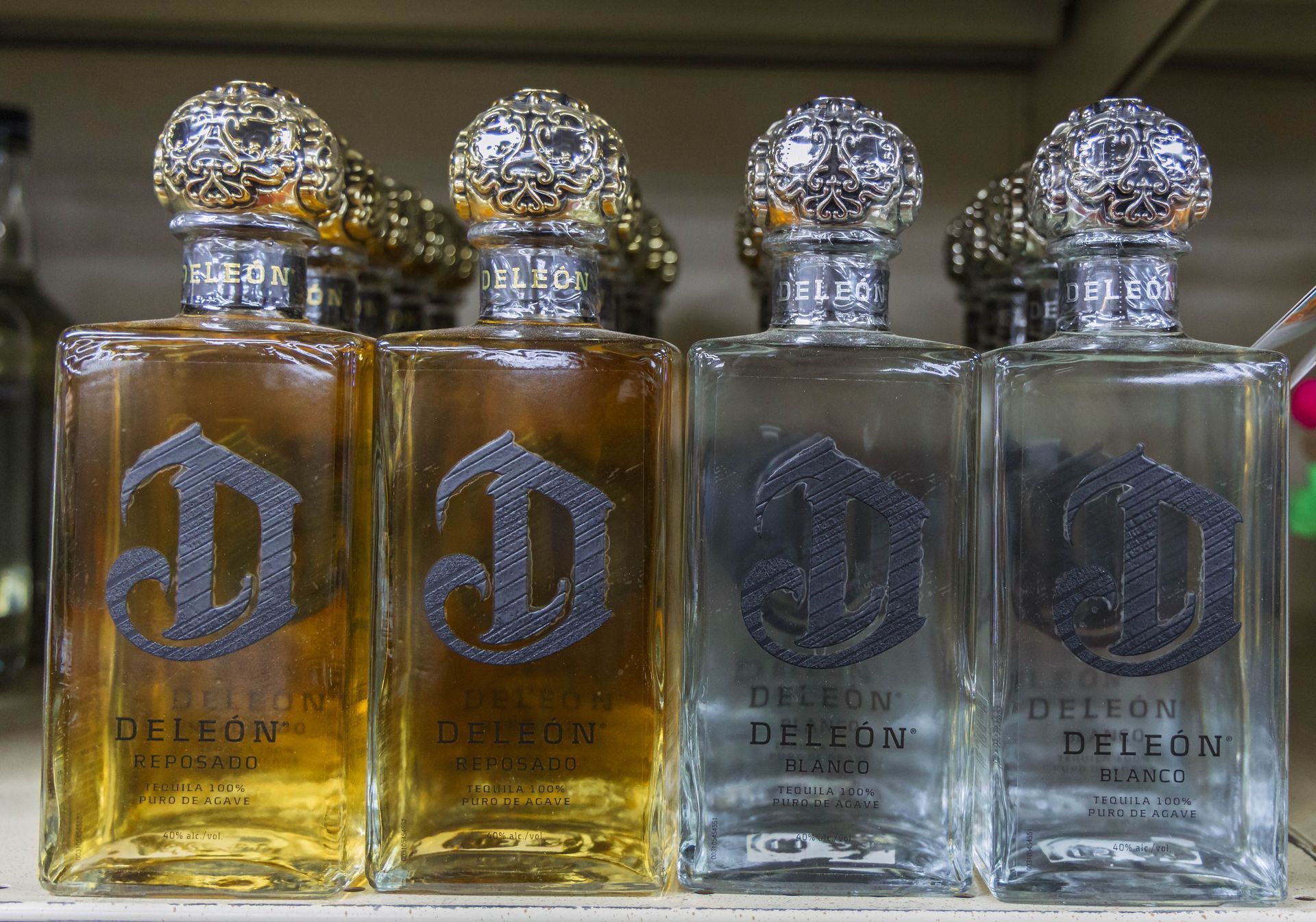 Bottles of Deleon tequila, amber and clear, with decorative silver stoppers and embossed logos.