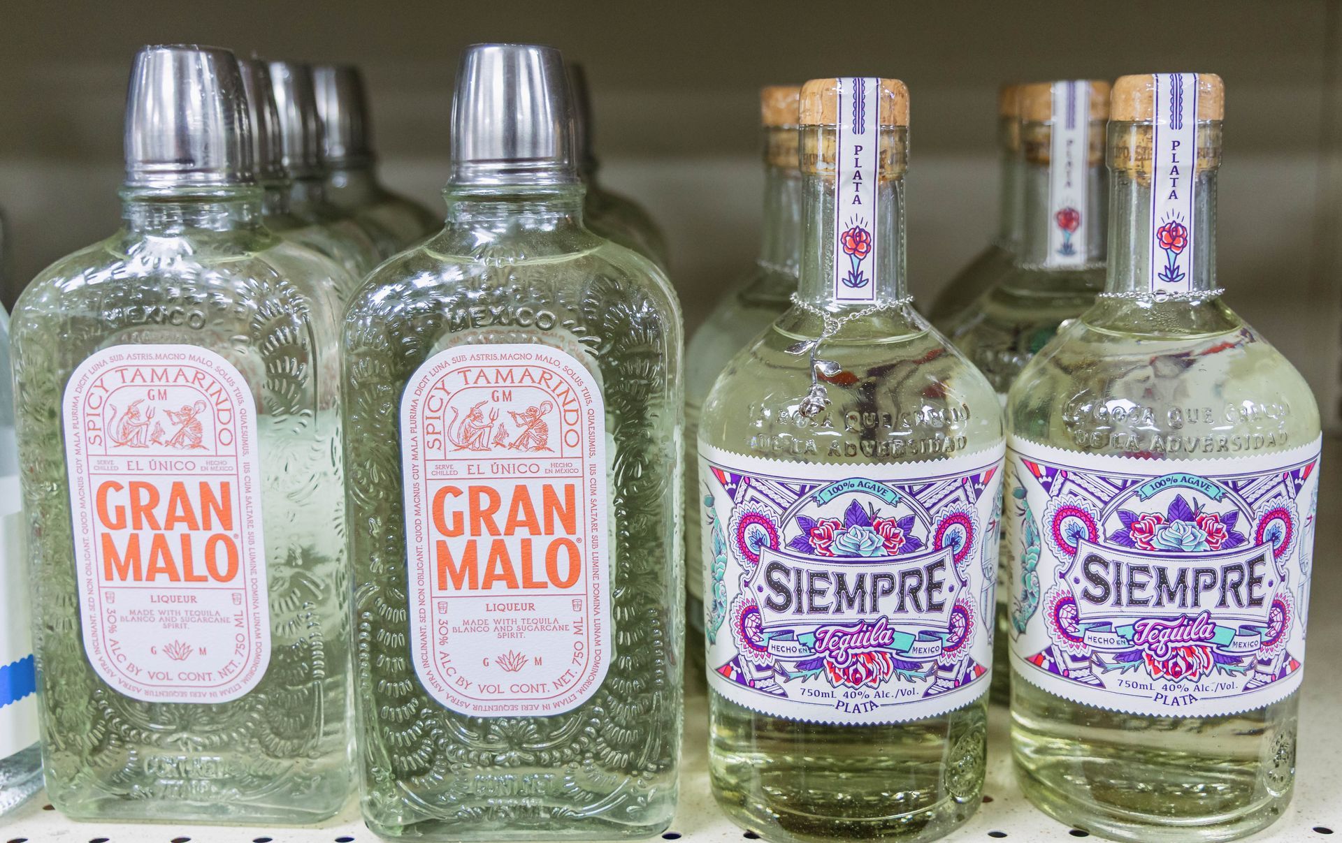 Bottles of Gran Malo and Siempre tequila on a store shelf, with distinctive labels and silver bottle caps.