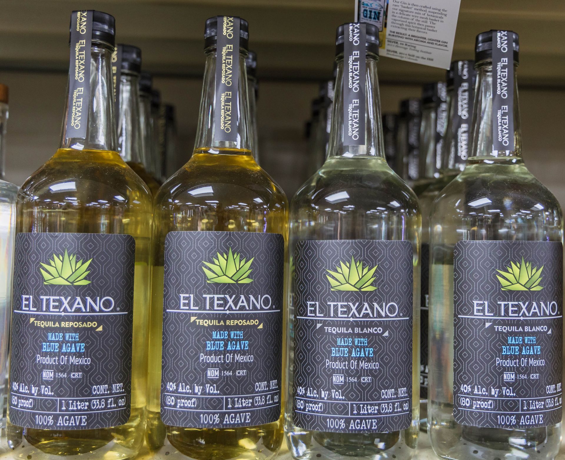 Four bottles of El Texano tequila on a shelf; labels in black and gray, varying shades of amber and clear liquid.