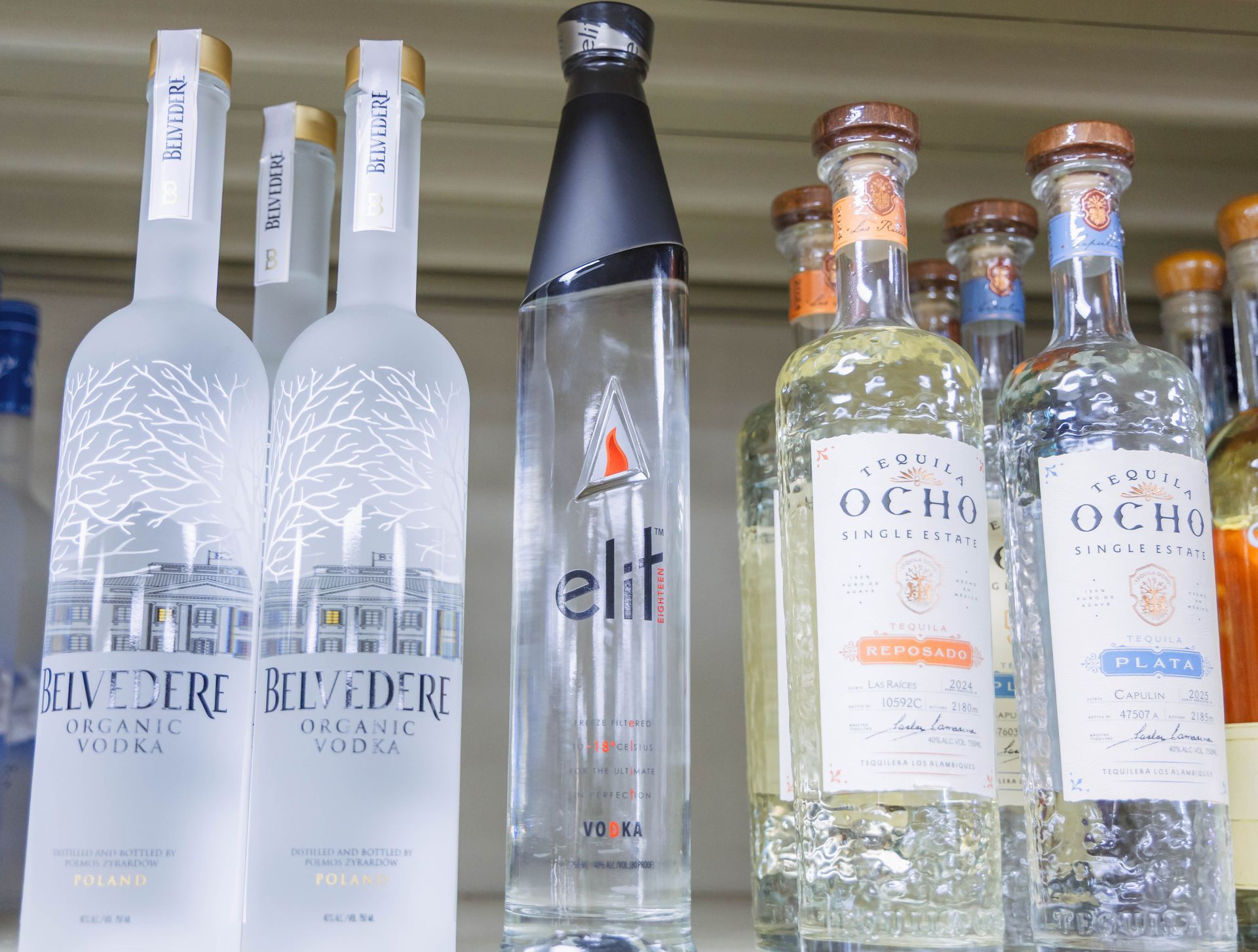 Bottles of vodka and tequila on a shelf, including Belvedere and Ocho brands.