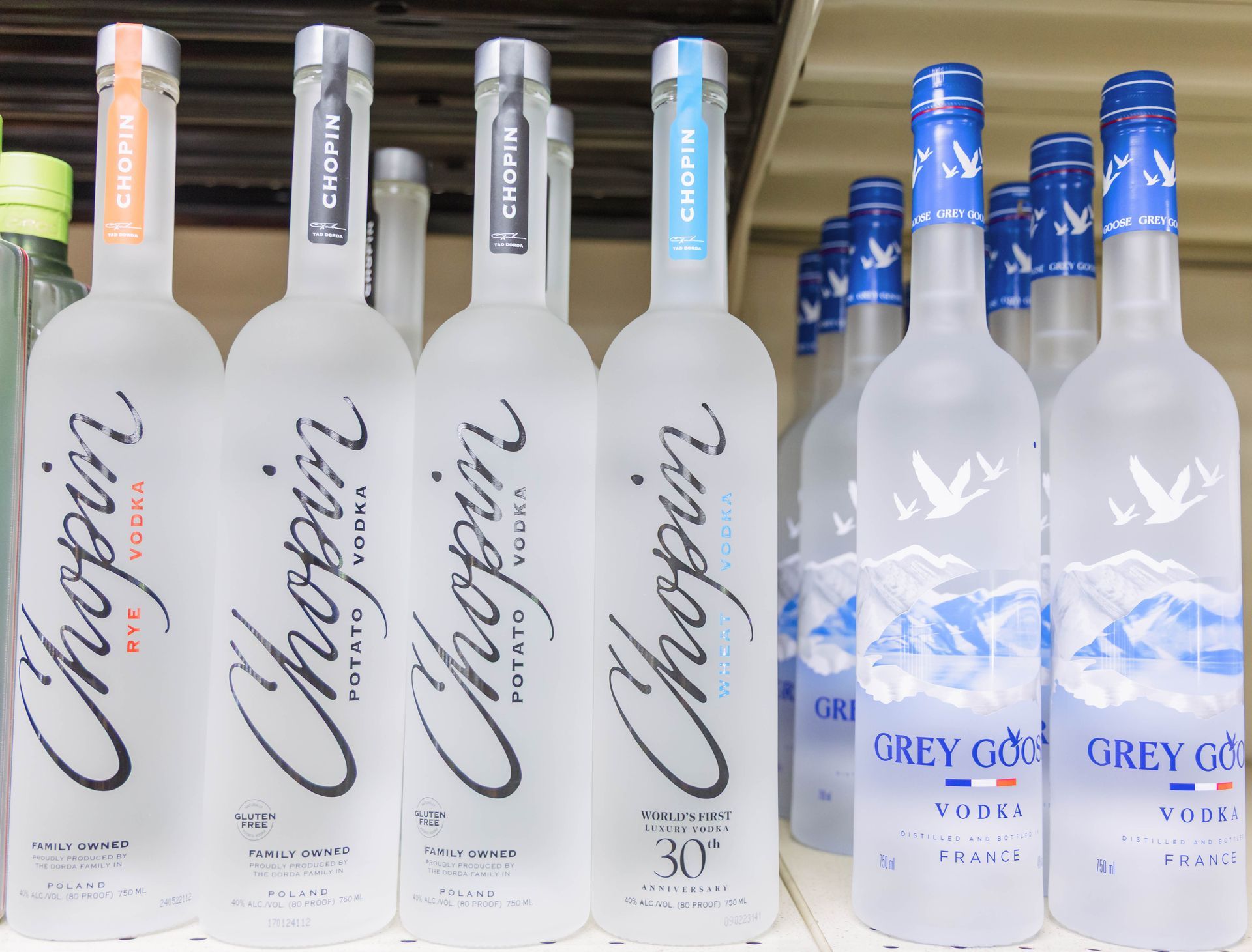 Bottles of Chopin and Grey Goose vodka on a shelf, various colors and labels.