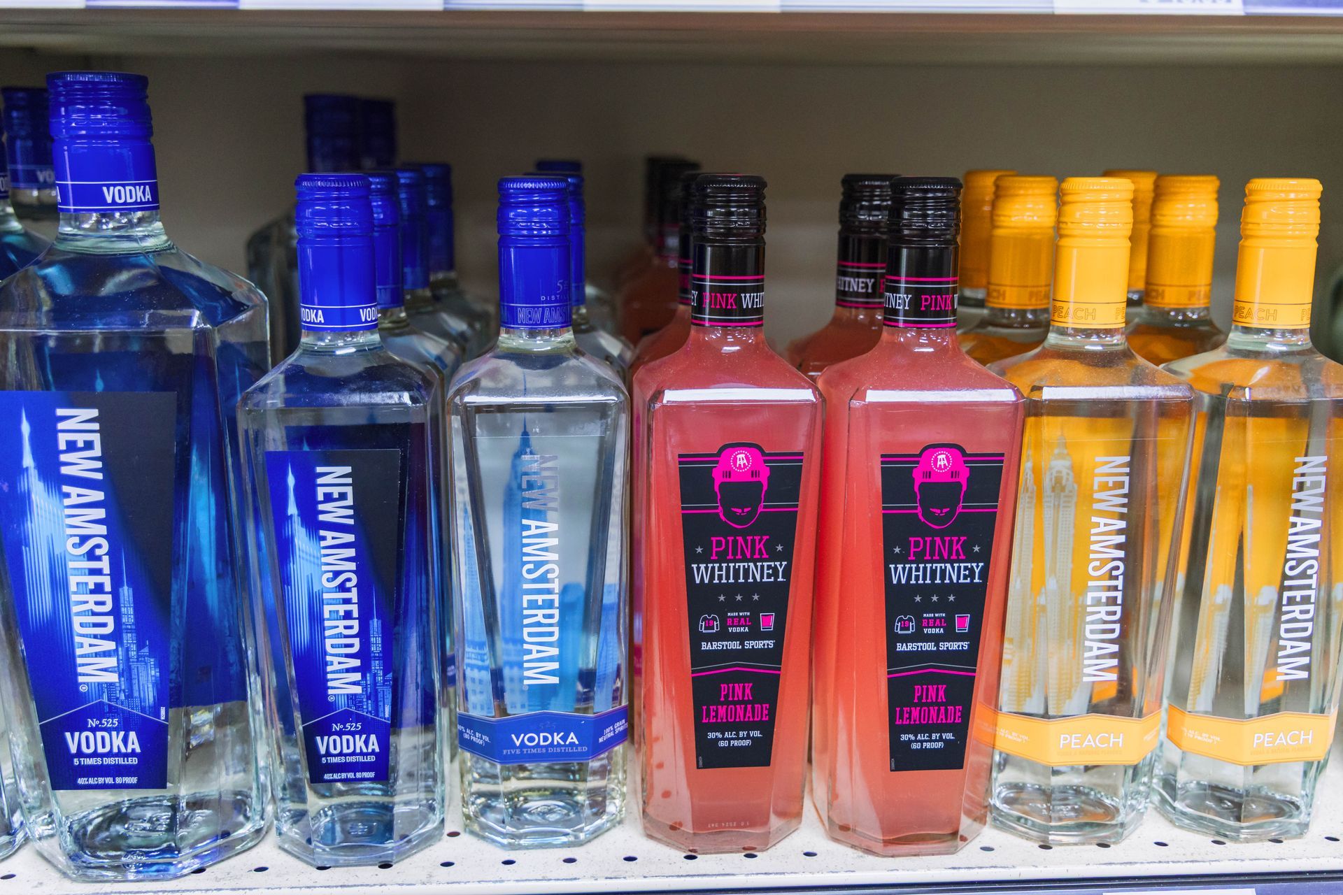 Bottles of vodka in various colors and flavors on a store shelf, including blue, pink, and orange.