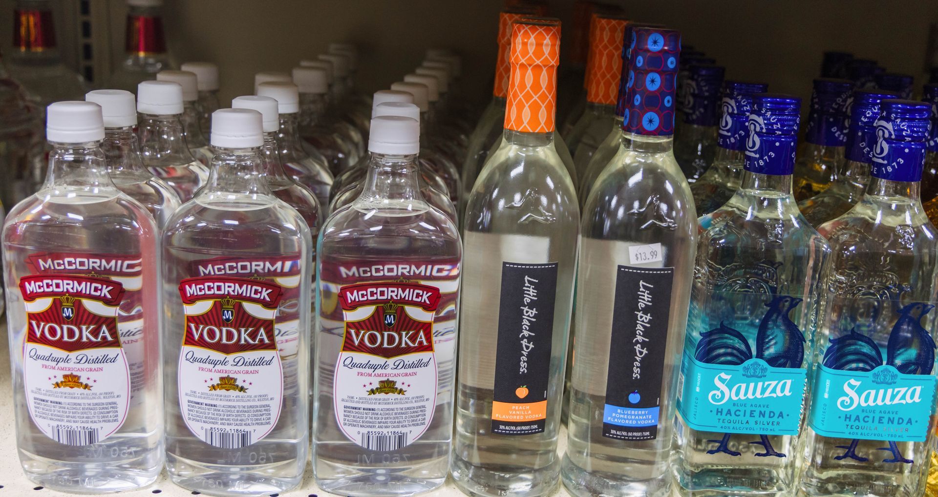 Bottles of vodka and tequila on a shelf in a store. Clear bottles with various labels and colorful foil tops.