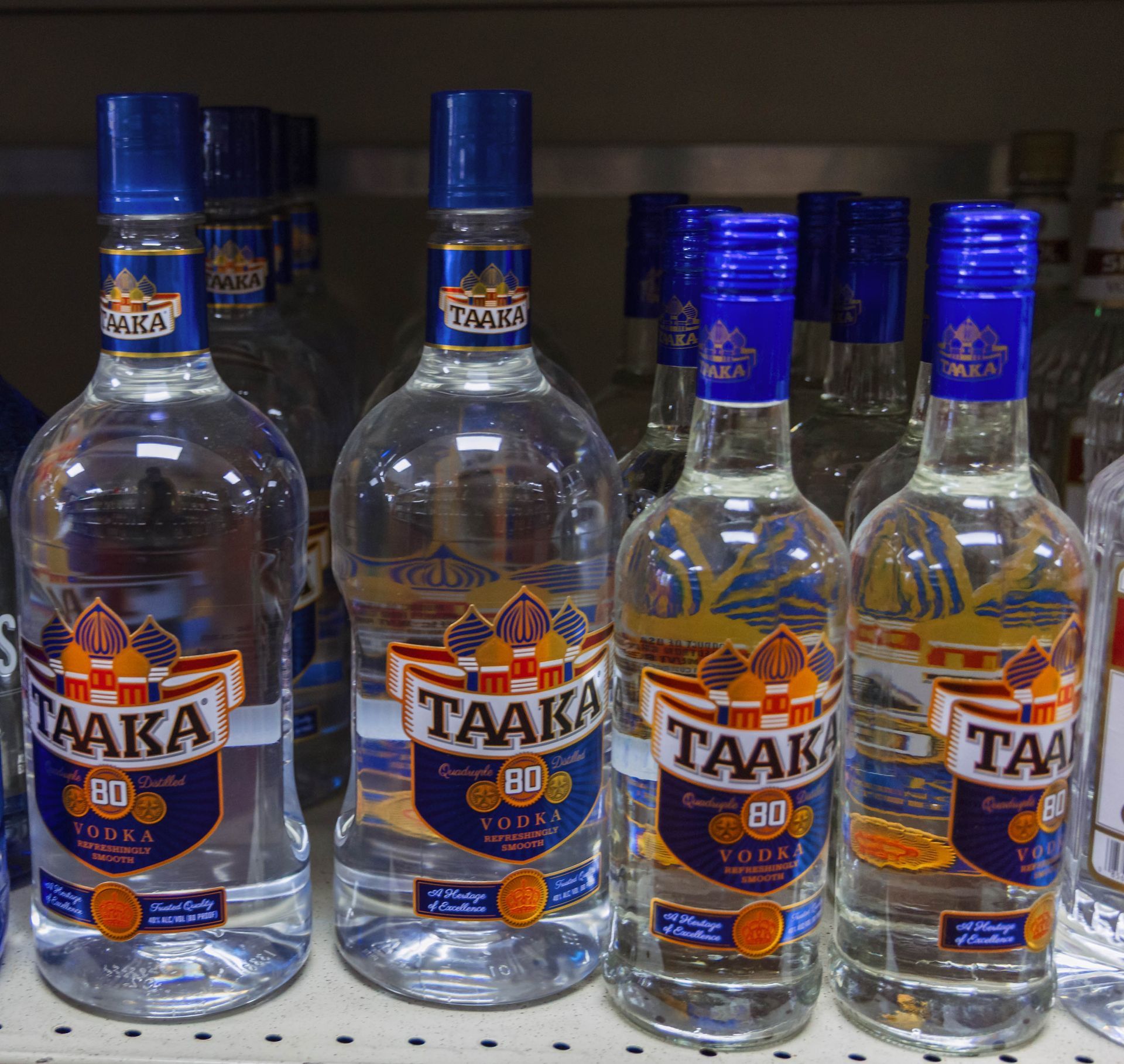 Bottles of Taaka 80 proof vodka on a shelf, blue and gold label.
