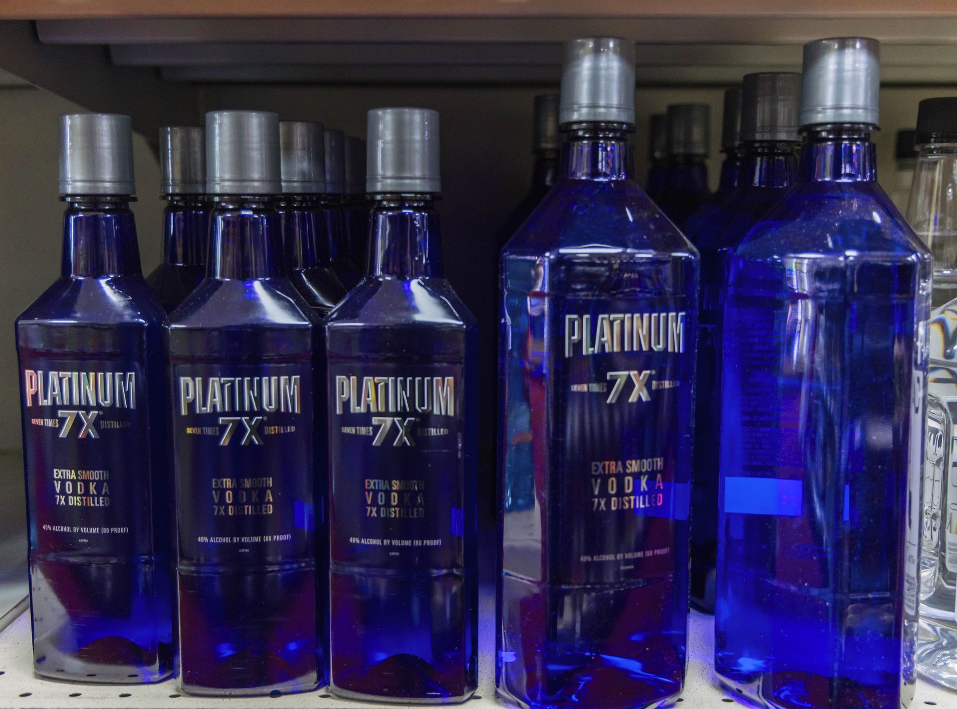 Bottles of blue Platinum 7X vodka on a shelf. Silver caps, silver text on a blue bottle.