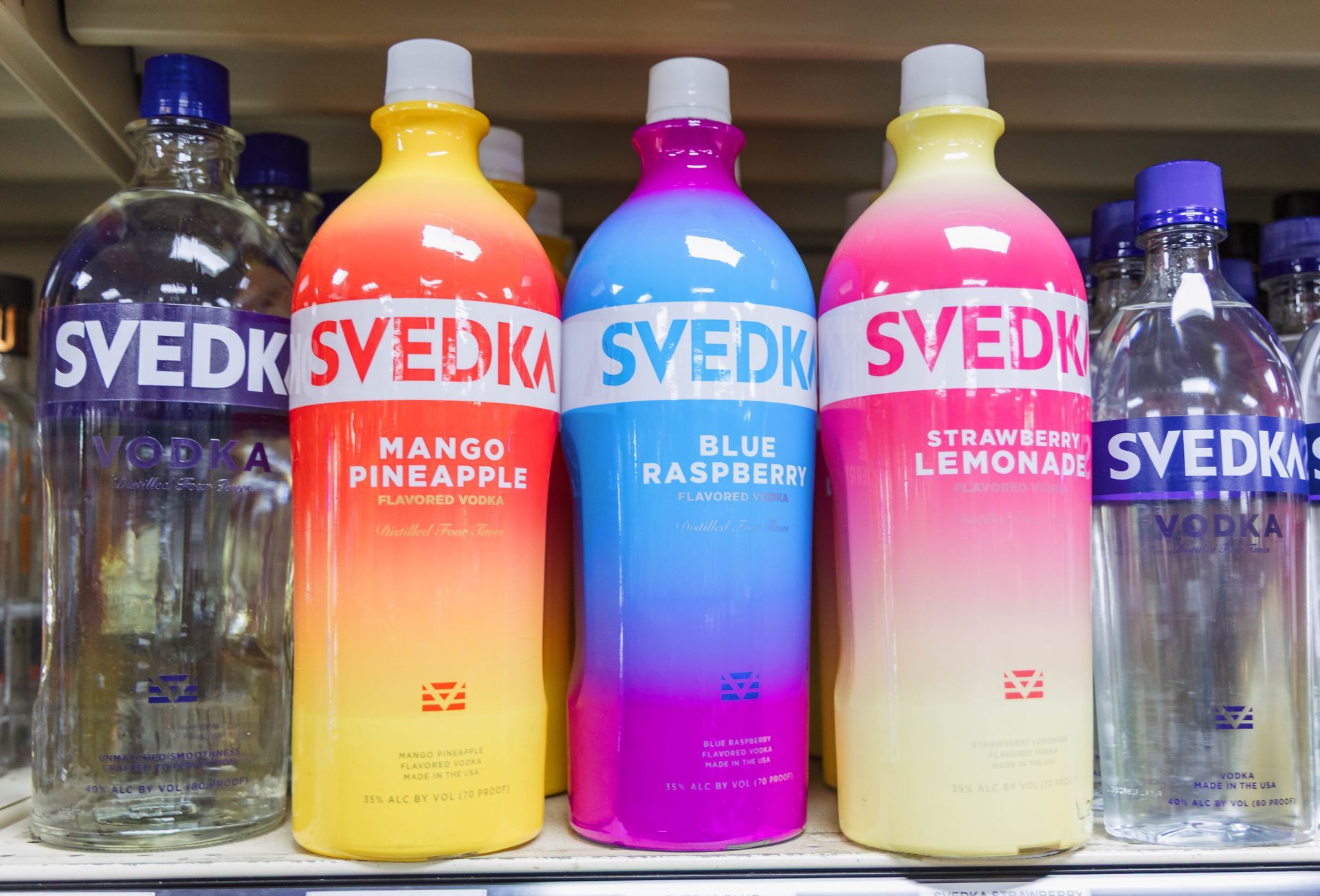 Svedka vodka bottles: Mango Pineapple, Blue Raspberry, Strawberry Lemonade. Colorful, on a shelf.