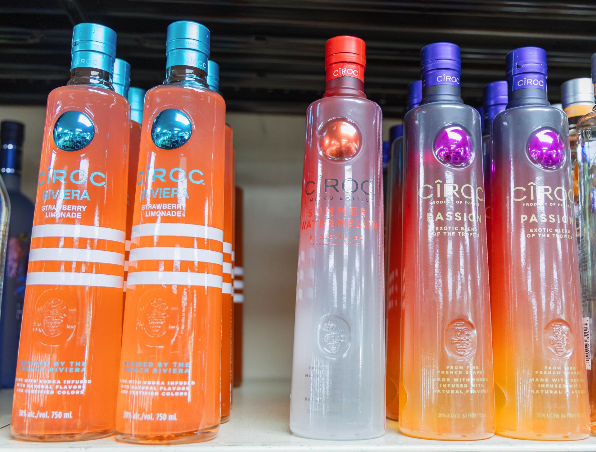 Bottles of Ciroc vodka in various fruit flavors, orange and purple gradient bottles on a shelf.