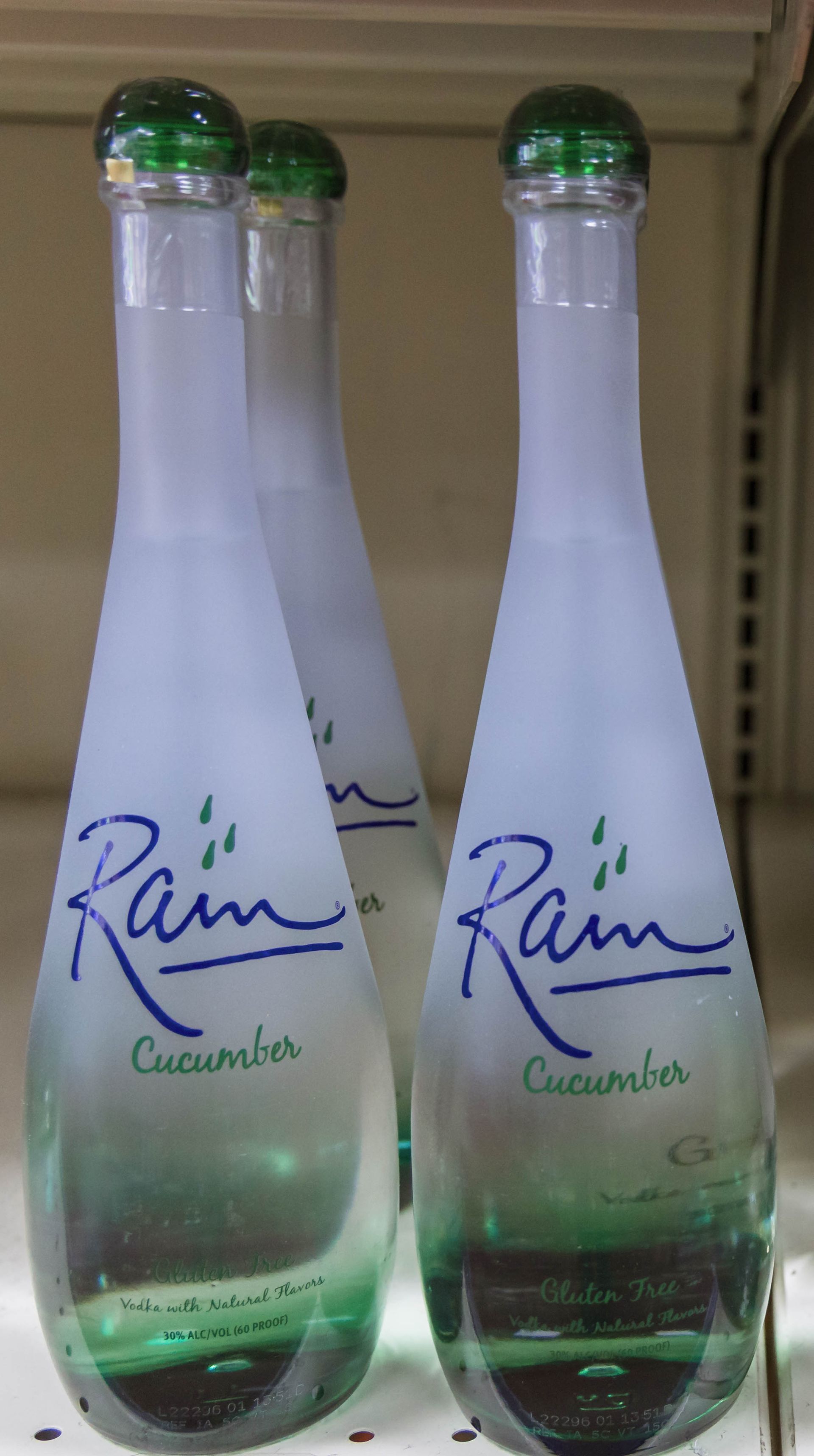Three Rain Cucumber water bottles, frosted glass, green caps, blue logo.
