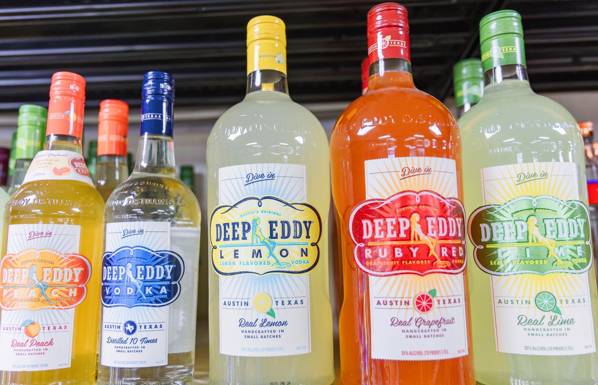 Bottles of Deep Eddy flavored vodka, arranged on a shelf. Flavors include peach, lemon, ruby red, and lime.