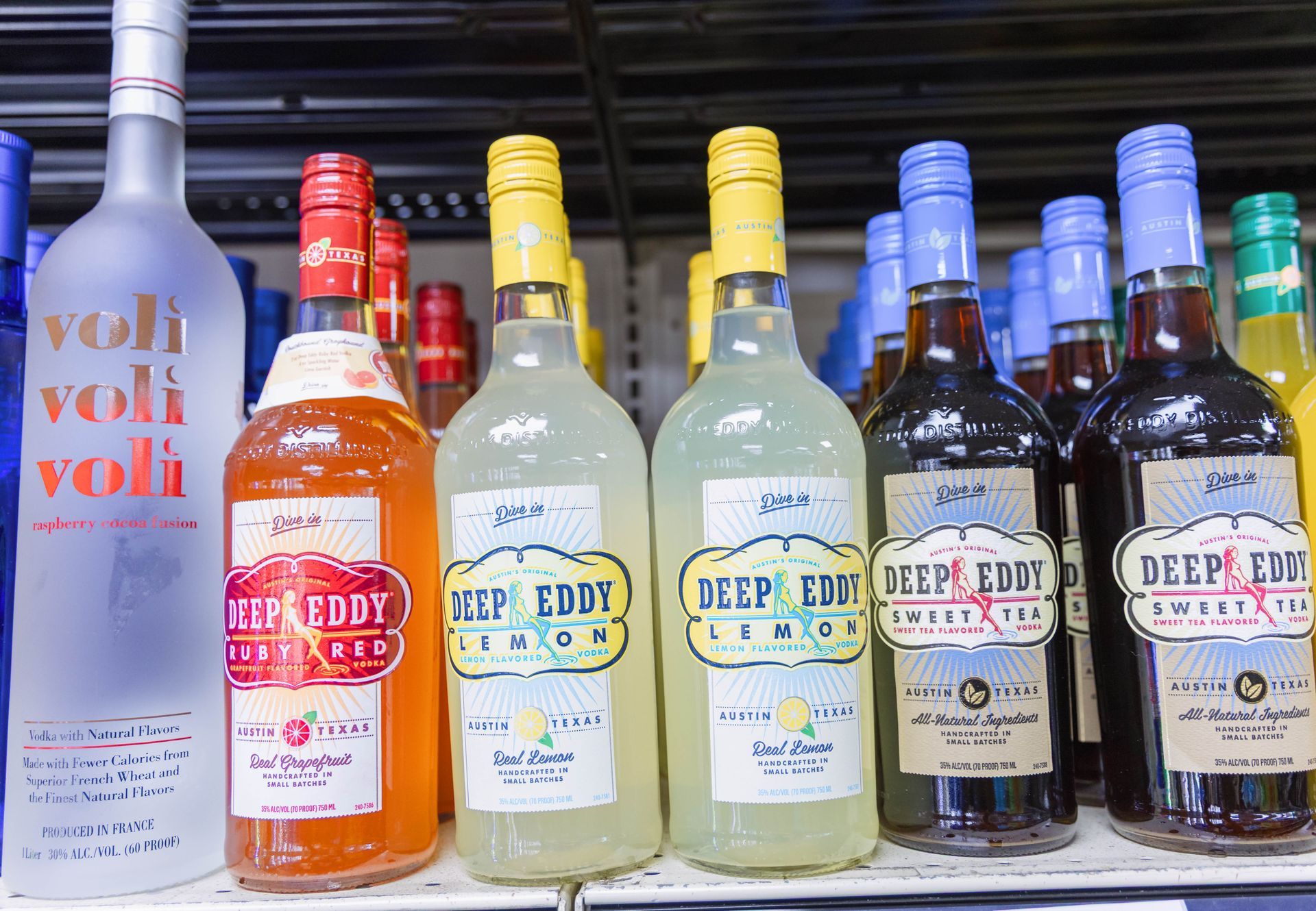 Bottles of alcoholic beverages on a shelf. Brands include Voli vodka and Deep Eddy flavored vodkas like lemon and cranberry.