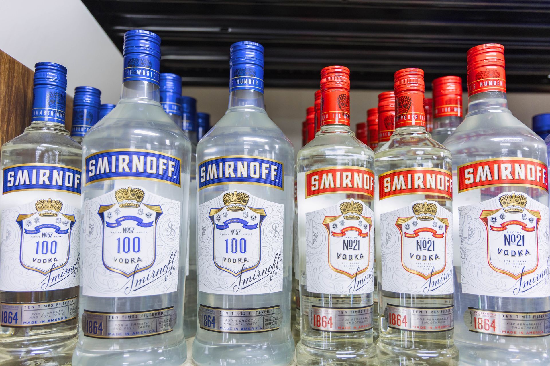 Bottles of Smirnoff vodka on a shelf; some with blue caps, others with red.