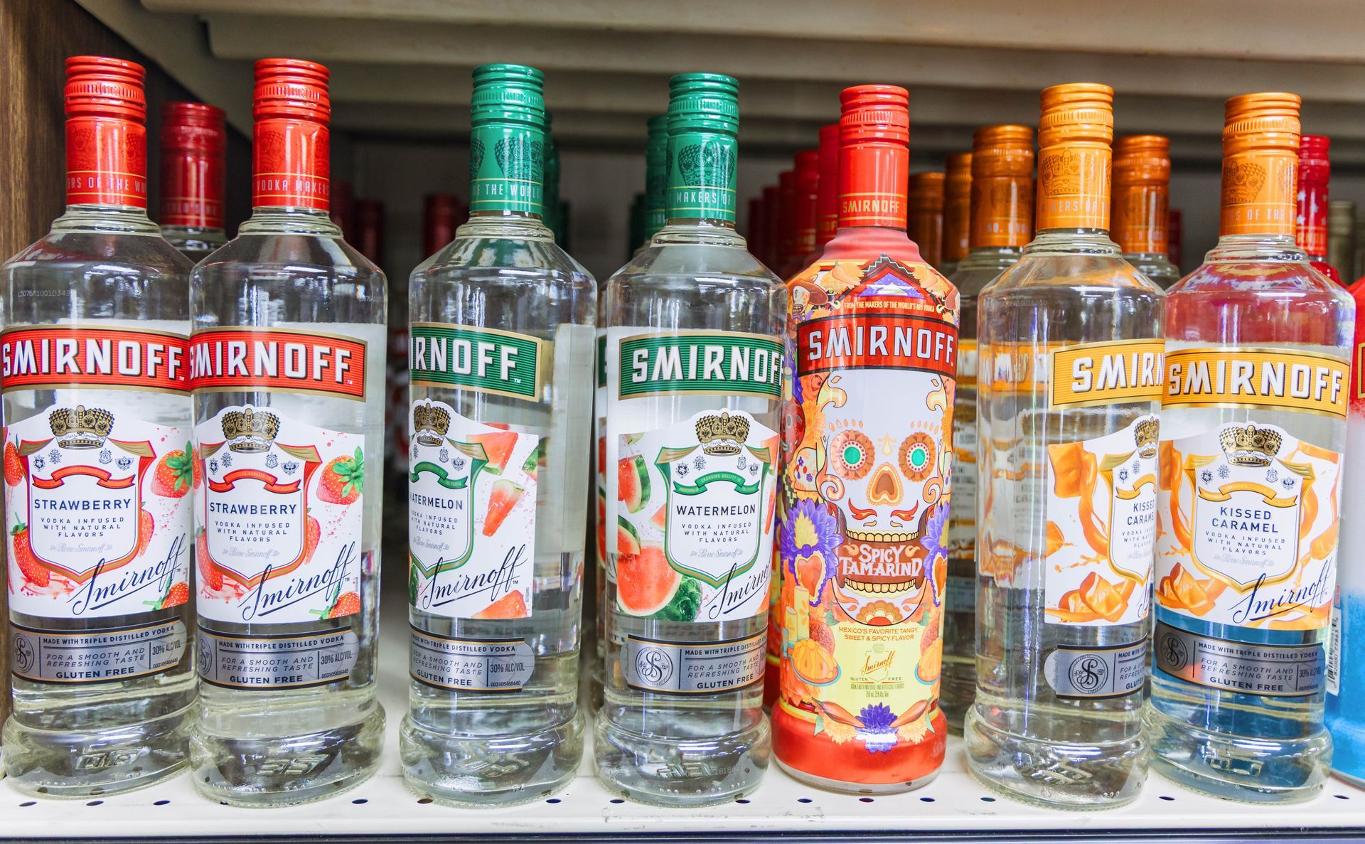 Bottles of Smirnoff vodka with various flavored labels on a shelf.