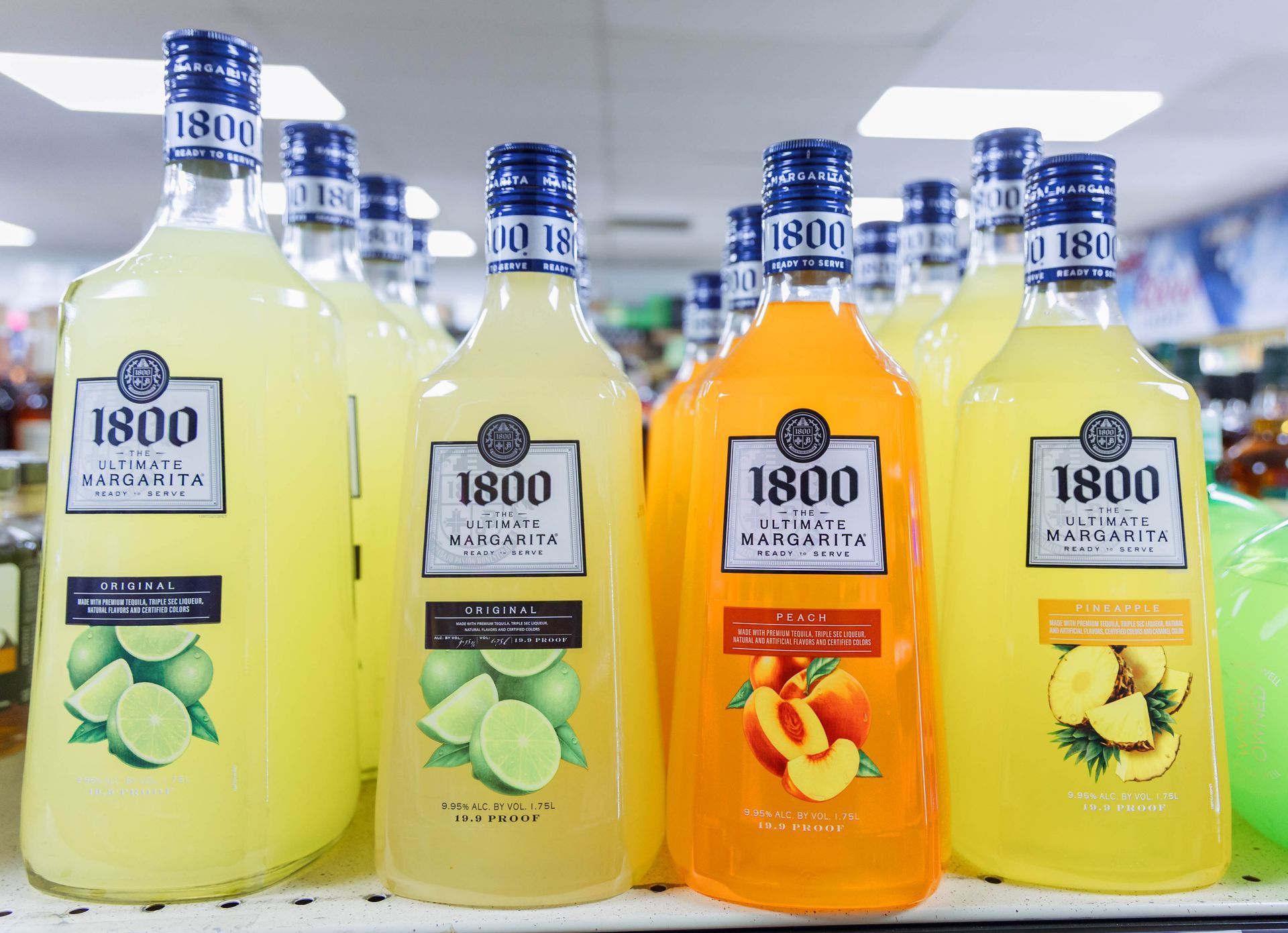 Bottles of 1800 Margarita, featuring lime, peach, and pineapple flavors, on a shelf in a liquor store.