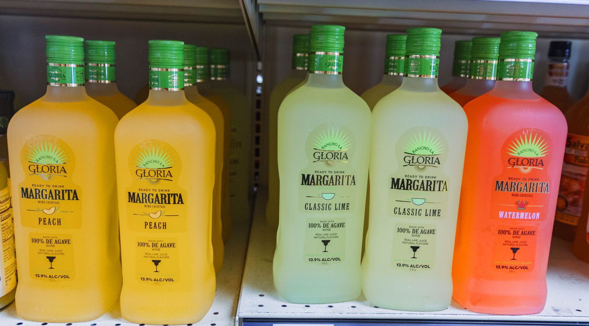 Bottles of pre-made margaritas in yellow, green, and orange, on a shelf in a store.