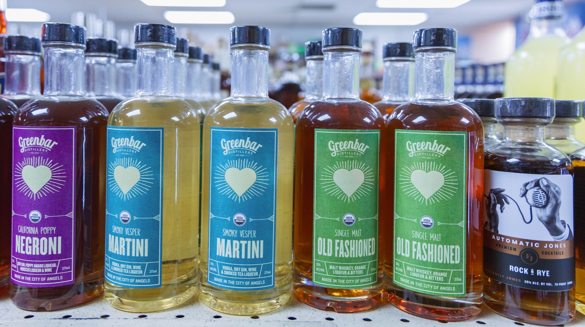Bottles of organic cocktail mixers on a shelf, with colorful labels featuring hearts.