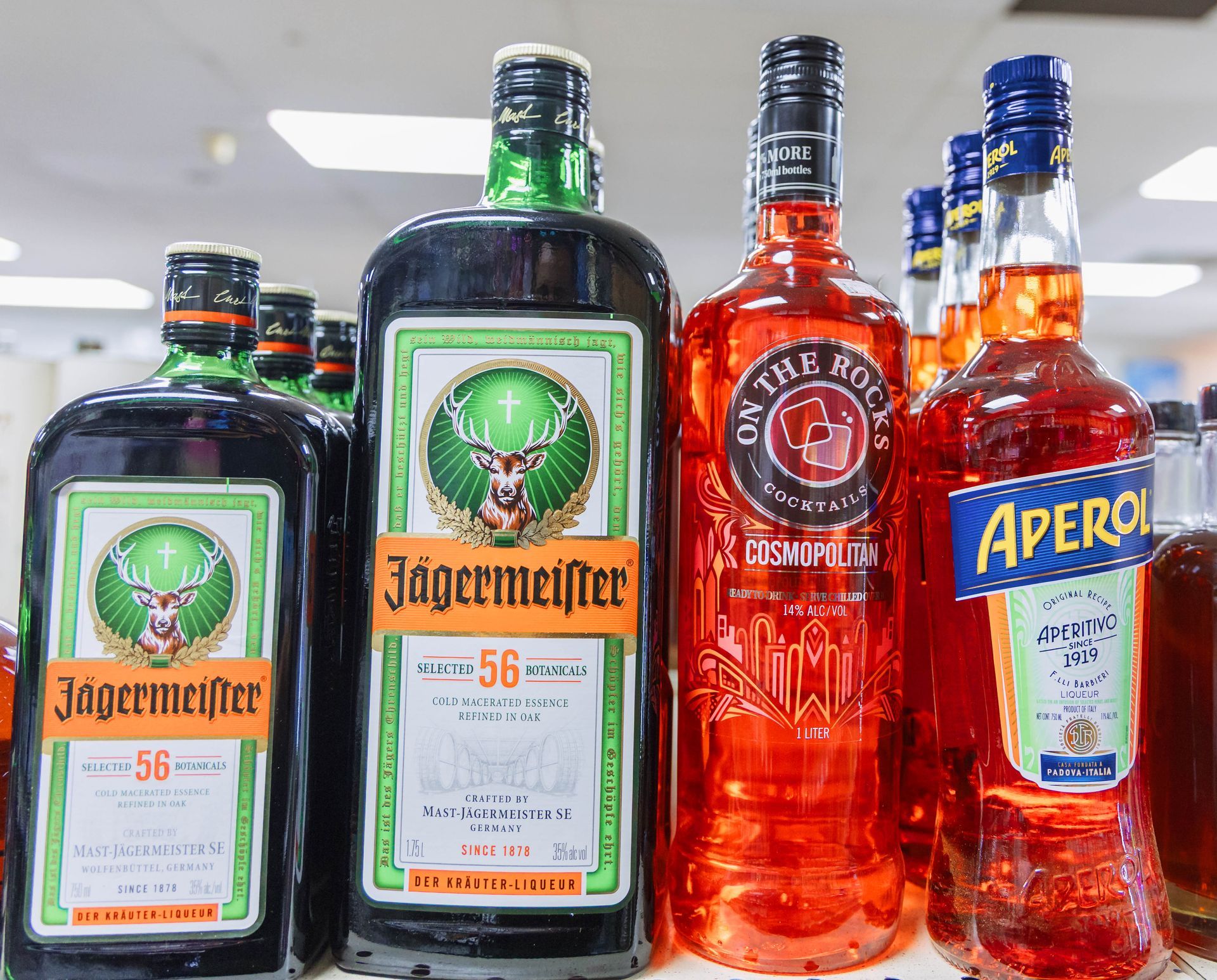 Bottles of various alcoholic beverages, including Jägermeister and Aperol, on a shelf.