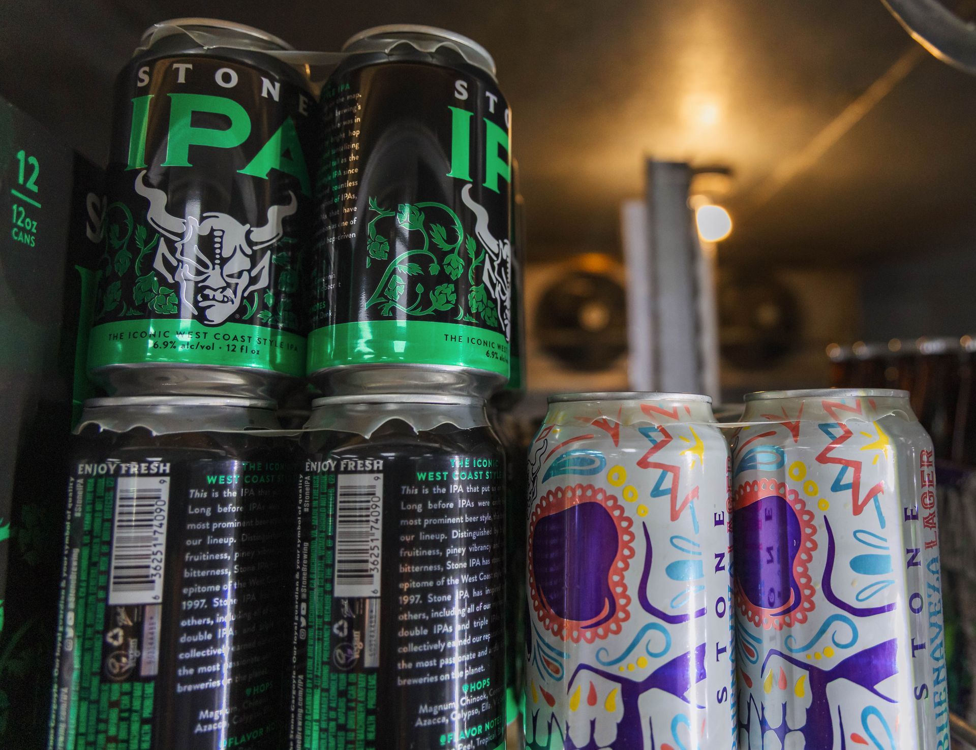 Canned beer in a cooler, featuring Stone IPA and a Day of the Dead design, stacked for sale.