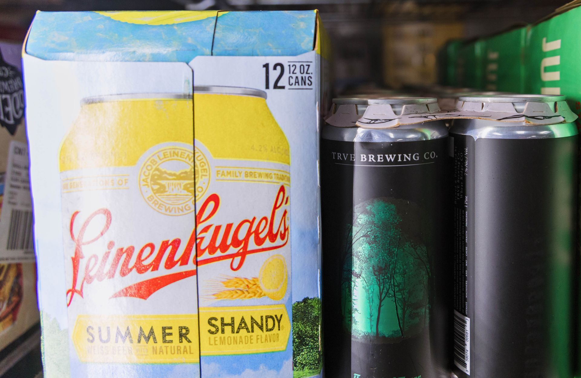 Leinenkugel's Summer Shandy 12-pack in cooler, next to other beer cans. Yellow and white packaging.