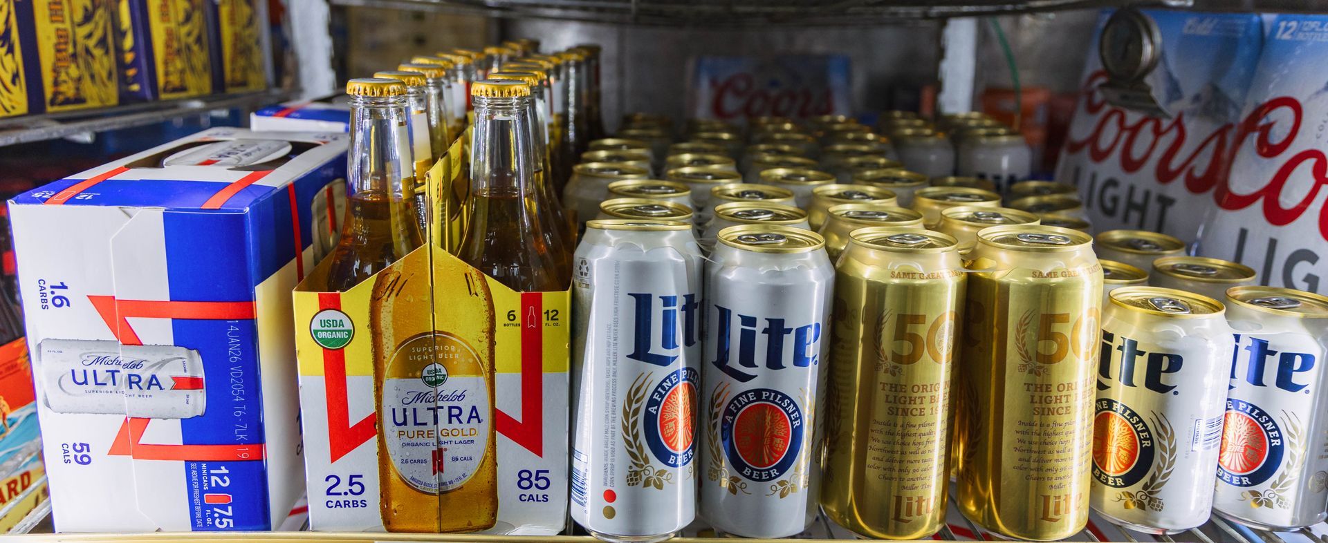 A refrigerator shelf stocked with various beer brands, including Bud Light, Miller Lite, and Coors Light.