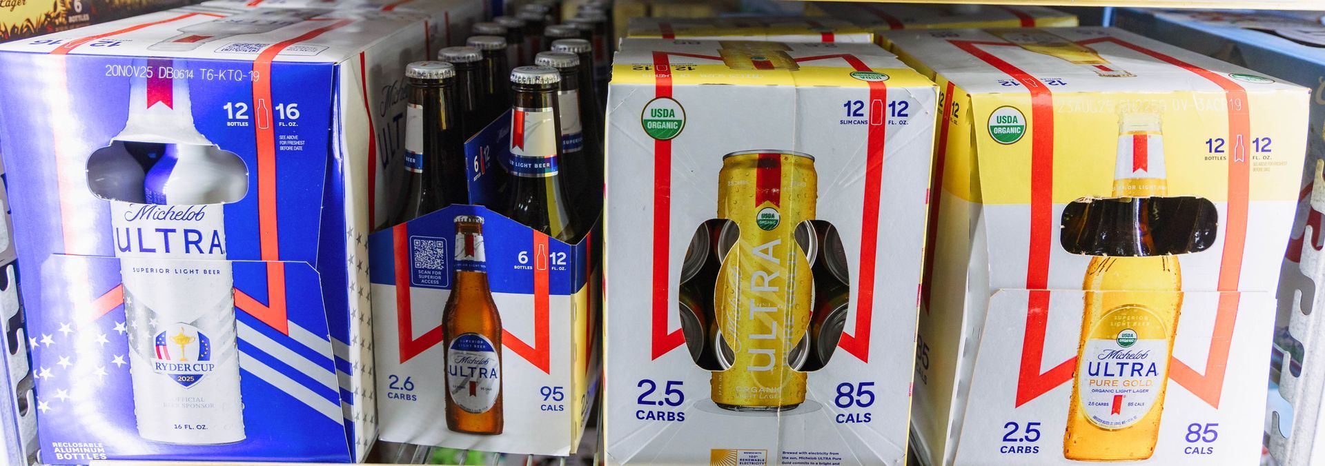 Cases of beer in a refrigerated display. Boxes have red, blue, and yellow color schemes.