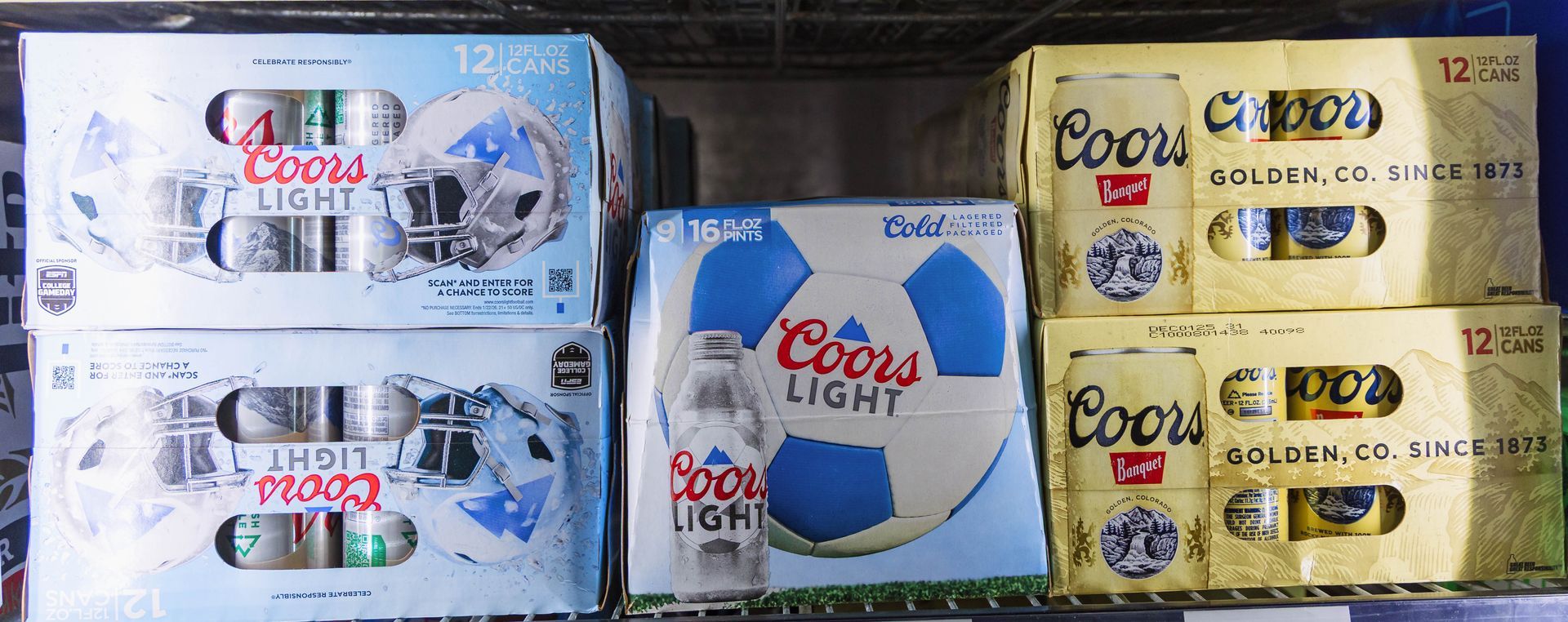 Cases of Coors Light and Coors beer in a store shelf, with soccer ball and vintage designs.