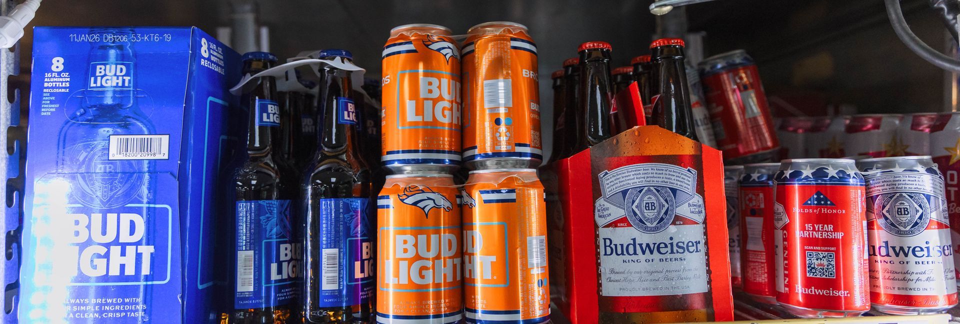 A shelf stocked with Bud Light, Budweiser, and other beer products in a cooler.