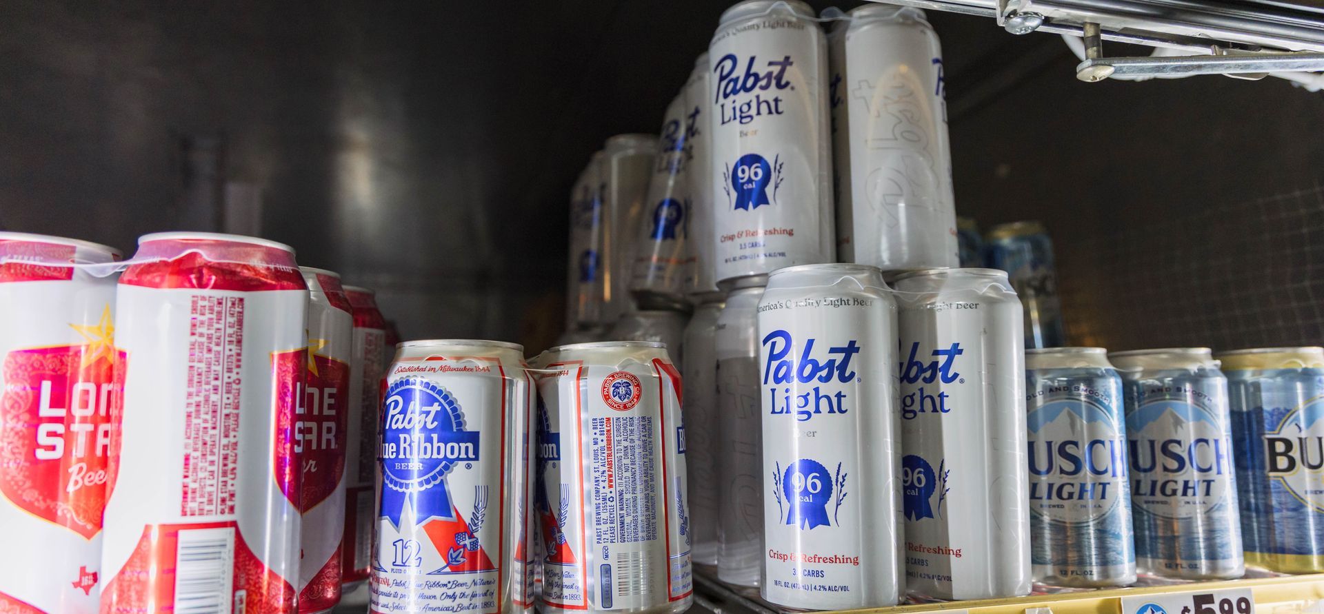 Cans of various beers, including Pabst Blue Ribbon Light and Lone Star, in a refrigerator.
