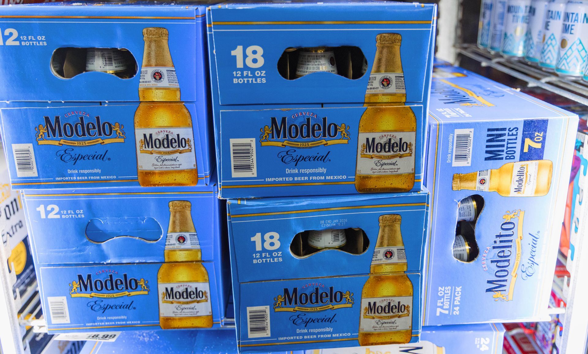 Cases of Modelo beer stacked in a store display, various sizes. Blue boxes with beer bottles visible.